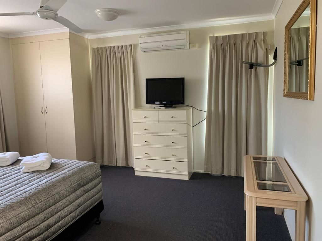 Bedroom with bed, dresser, TV, beige curtains, and wall mirror