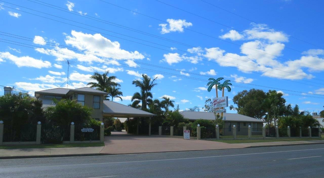 Single-story building with palm trees under a bright blue sky on a sunny street