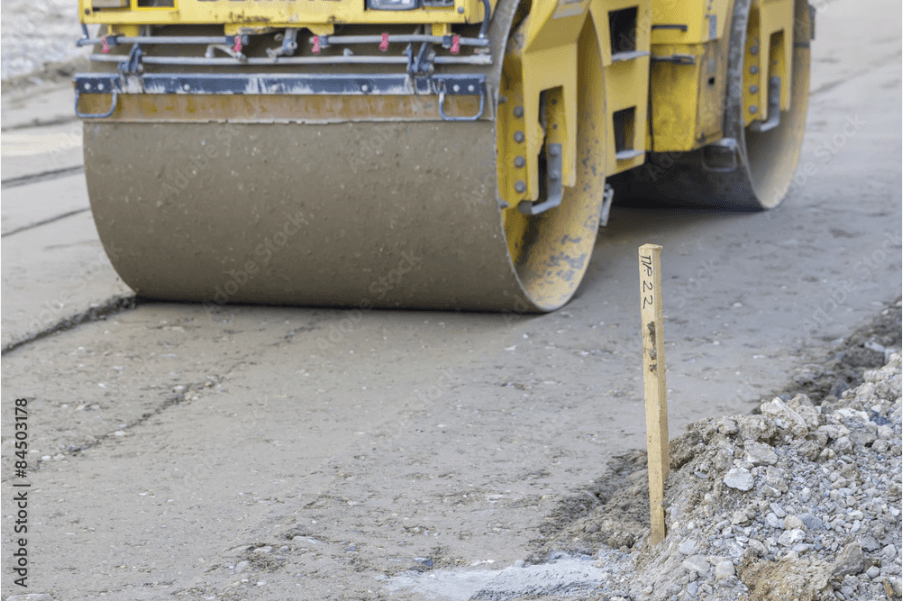 Construction equipment preparing road with survey stake visible