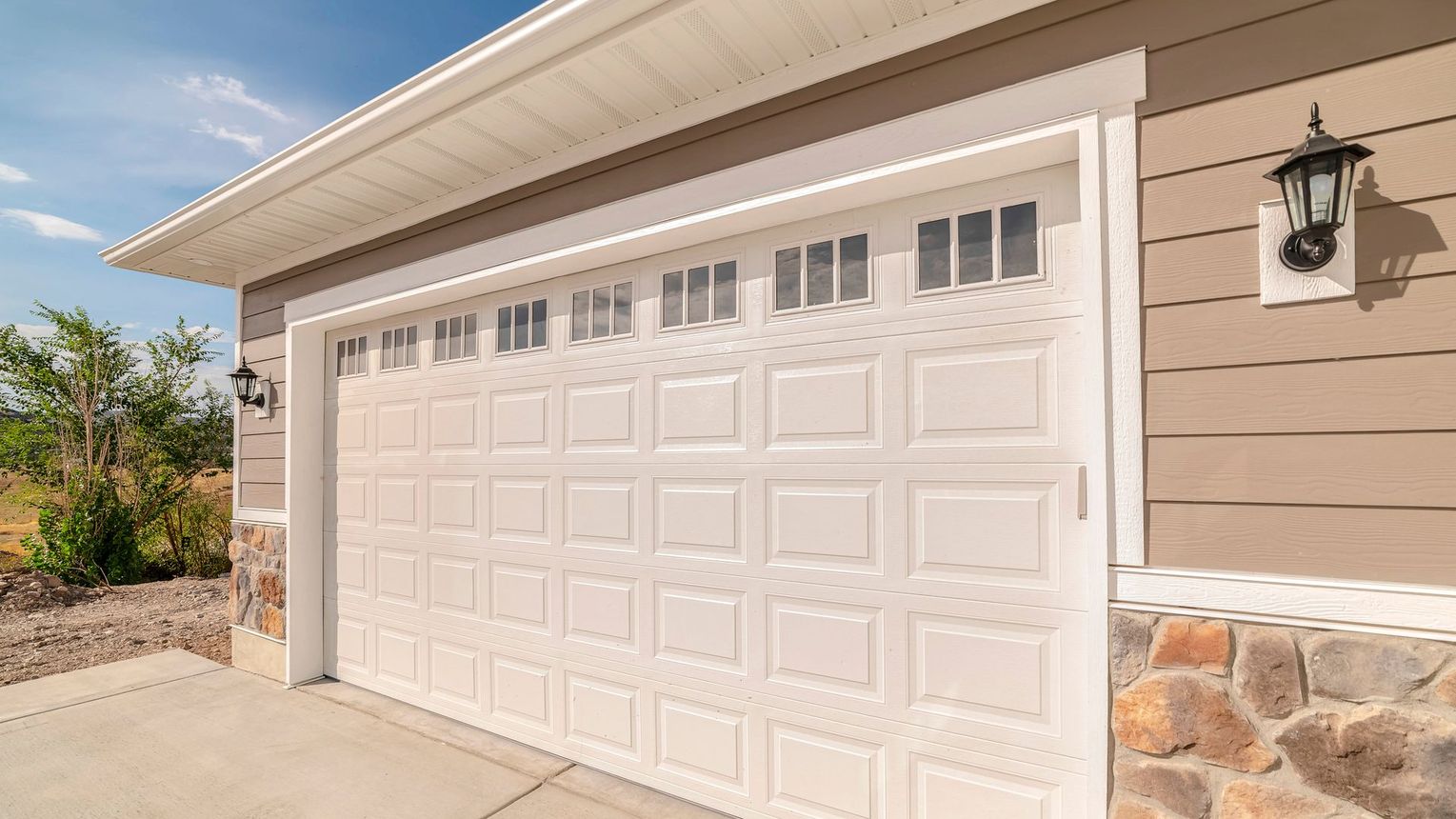 White garage door on a tan house with stone accents, topped with a white overhang.