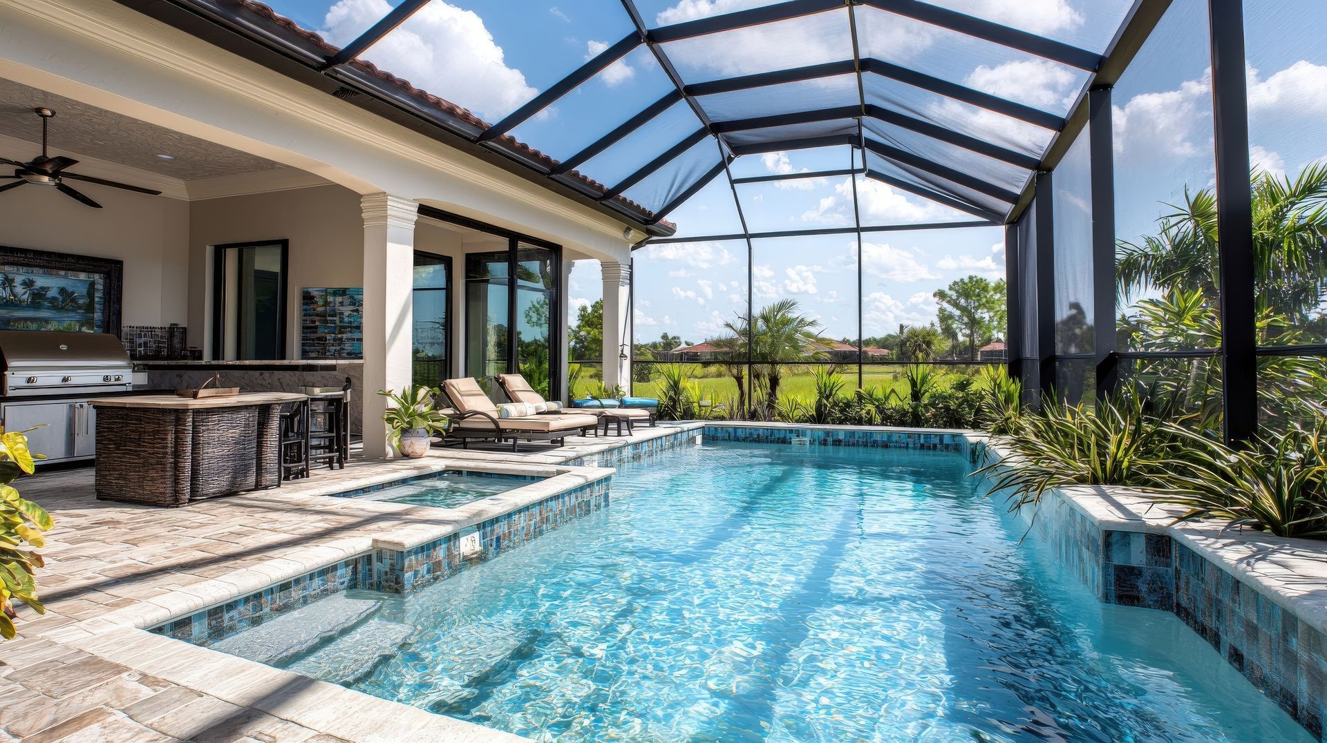 A rectangular swimming pool with a spa inside a screened lanai, next to an outdoor kitchen and lounge chairs. A rectangular swimming pool with a spa inside a screened lanai, next to an outdoor kitchen and lounge chairs.
