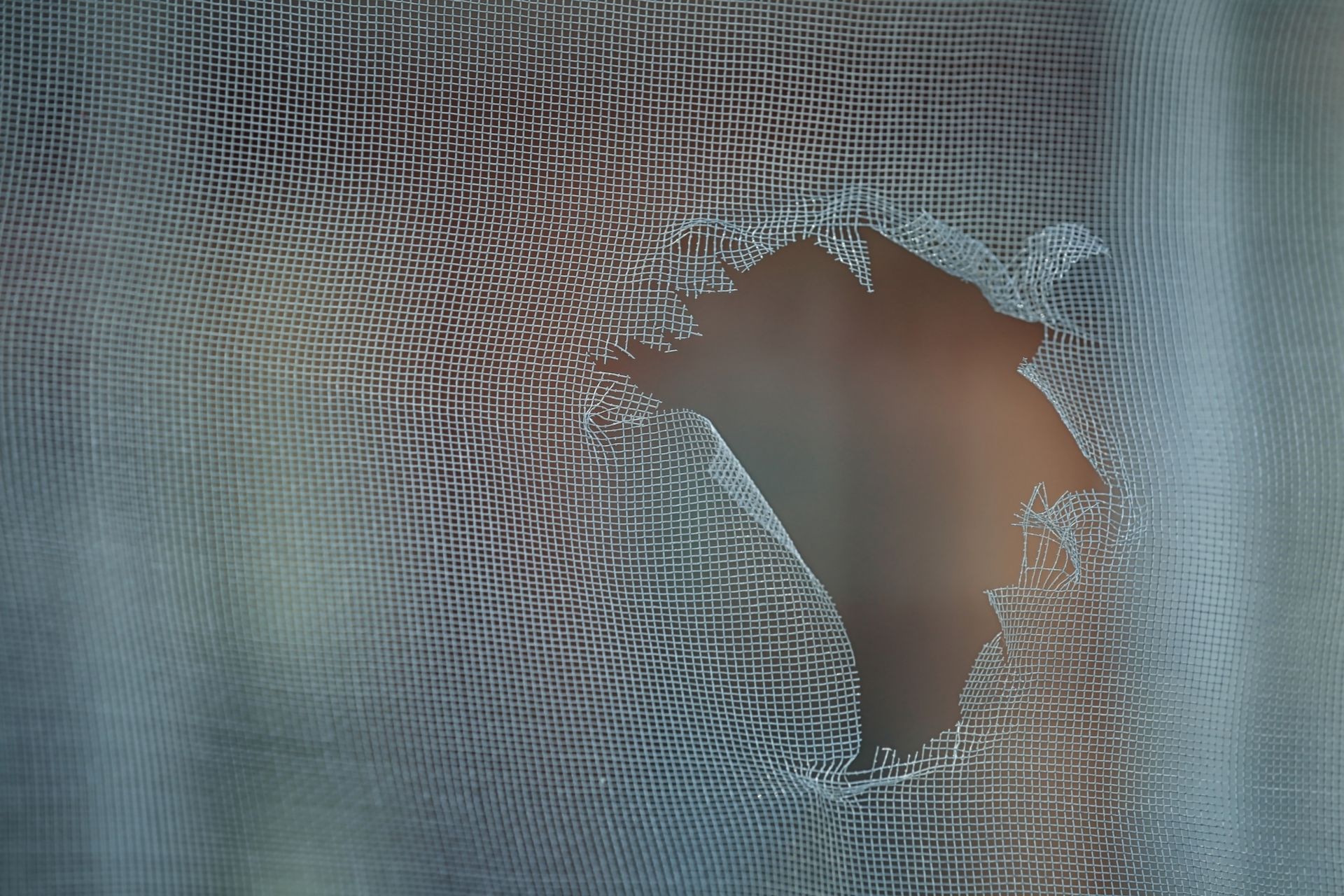 A close-up of a white mesh fabric with a large, irregular tear, revealing a smooth, blurred skin-tone background. A close-up of a white mesh fabric with a large, irregular tear, revealing a smooth, blurred skin-tone background.