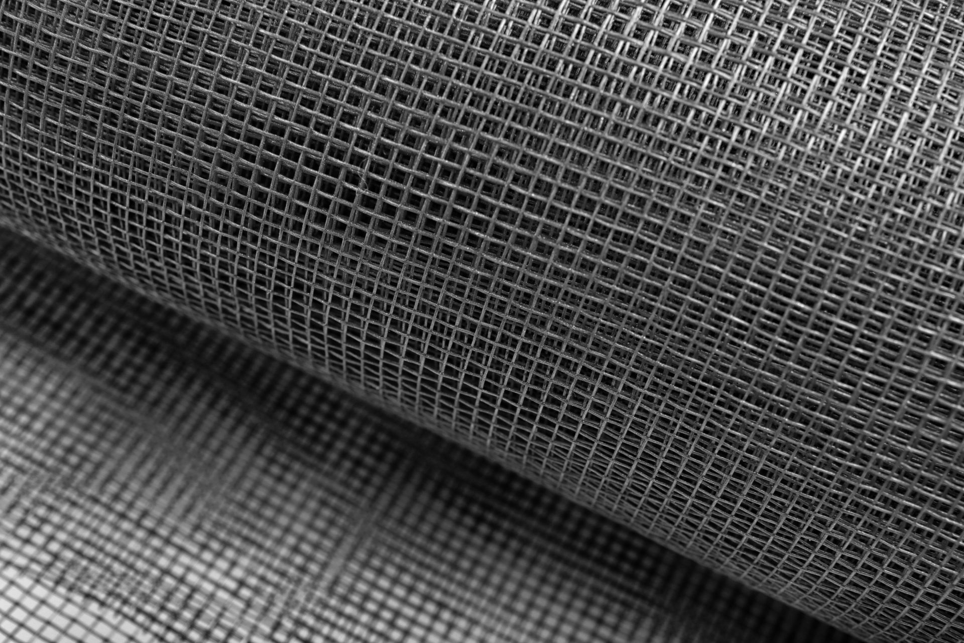 A close-up, angled view of dark grey, fine-mesh screening material with a consistent, grid-like woven pattern. A close-up, angled view of dark grey, fine-mesh screening material with a consistent, grid-like woven pattern.
