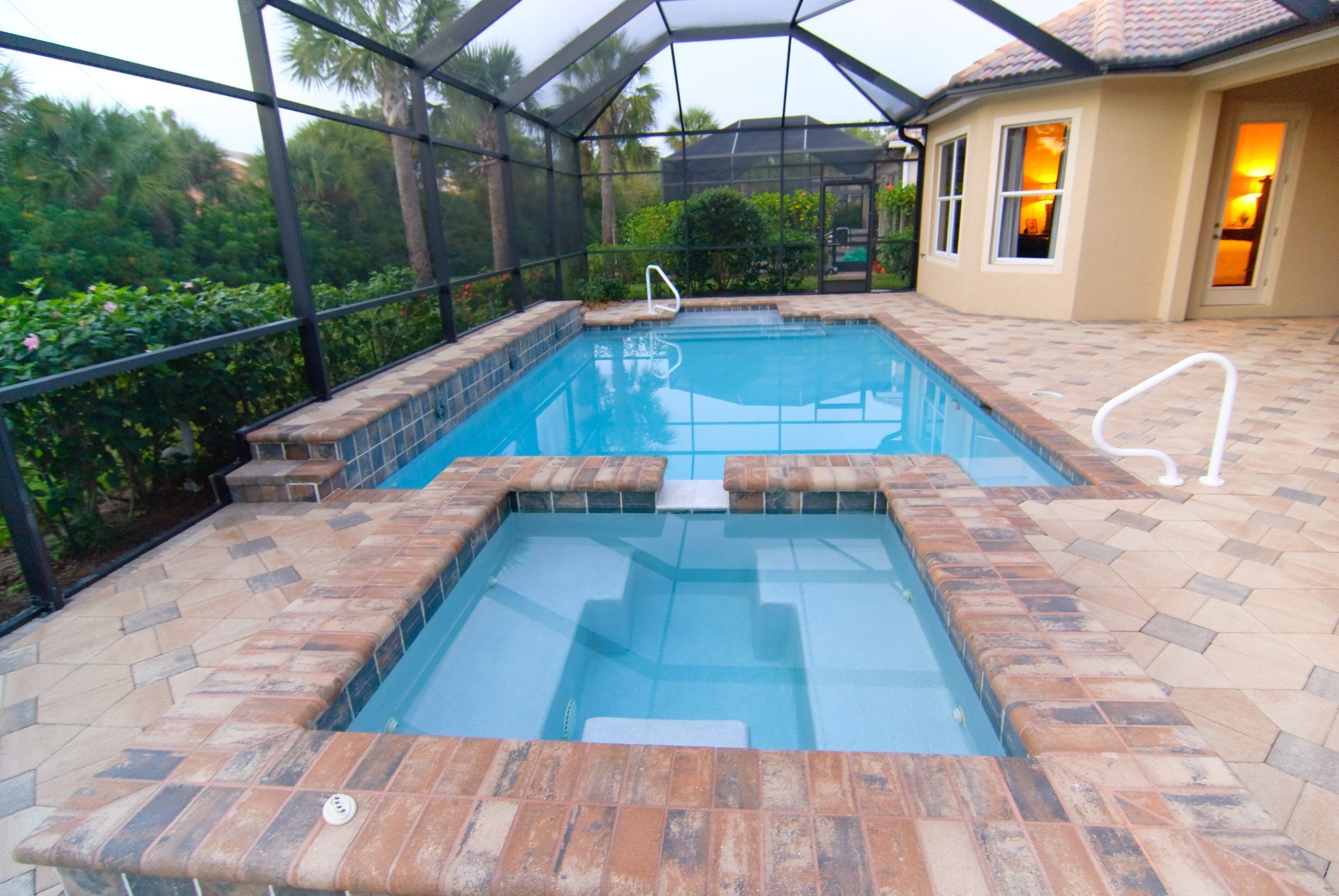 A rectangular swimming pool and attached hot tub on a brick patio, enclosed by a screened-in lanai at a home. A rectangular swimming pool and attached hot tub on a brick patio, enclosed by a screened-in lanai at a home.