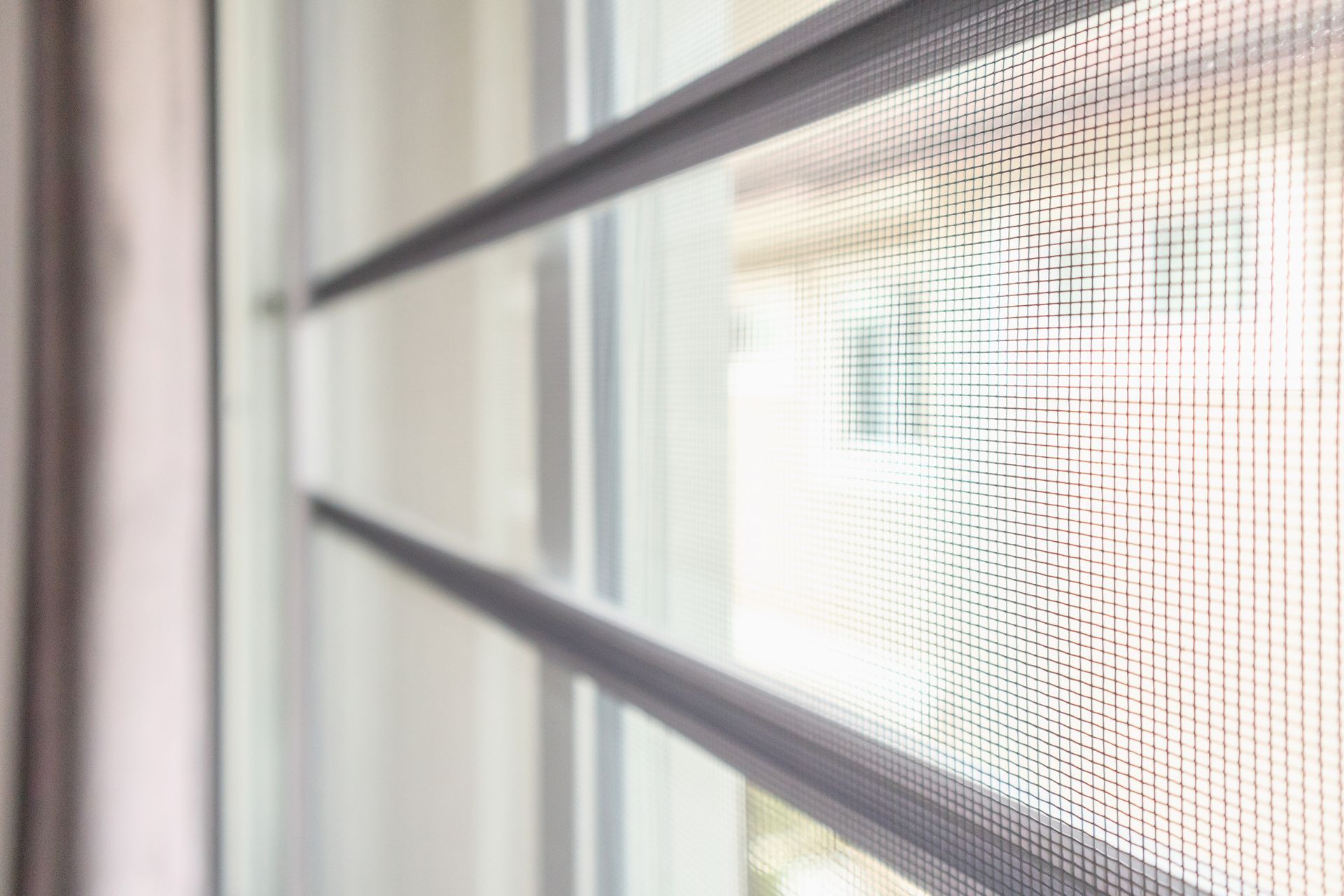 Close-up of a window screen with a gray frame and mesh, with a blurred view of the exterior visible through the window.