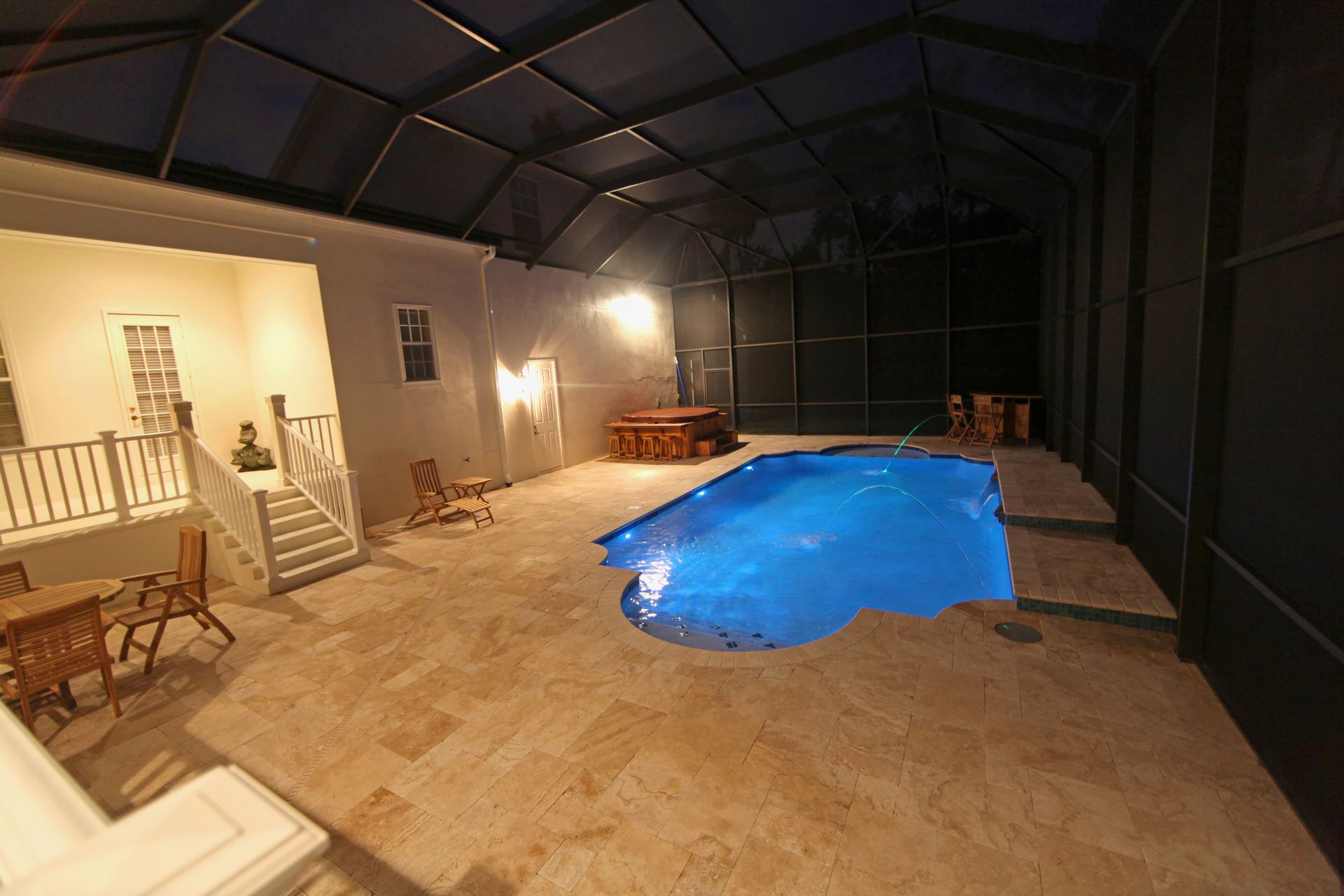 A lit outdoor pool area at night, featuring a blue-lit swimming pool on a stone patio inside a screened enclosure. A lit outdoor pool area at night, featuring a blue-lit swimming pool on a stone patio inside a screened enclosure.