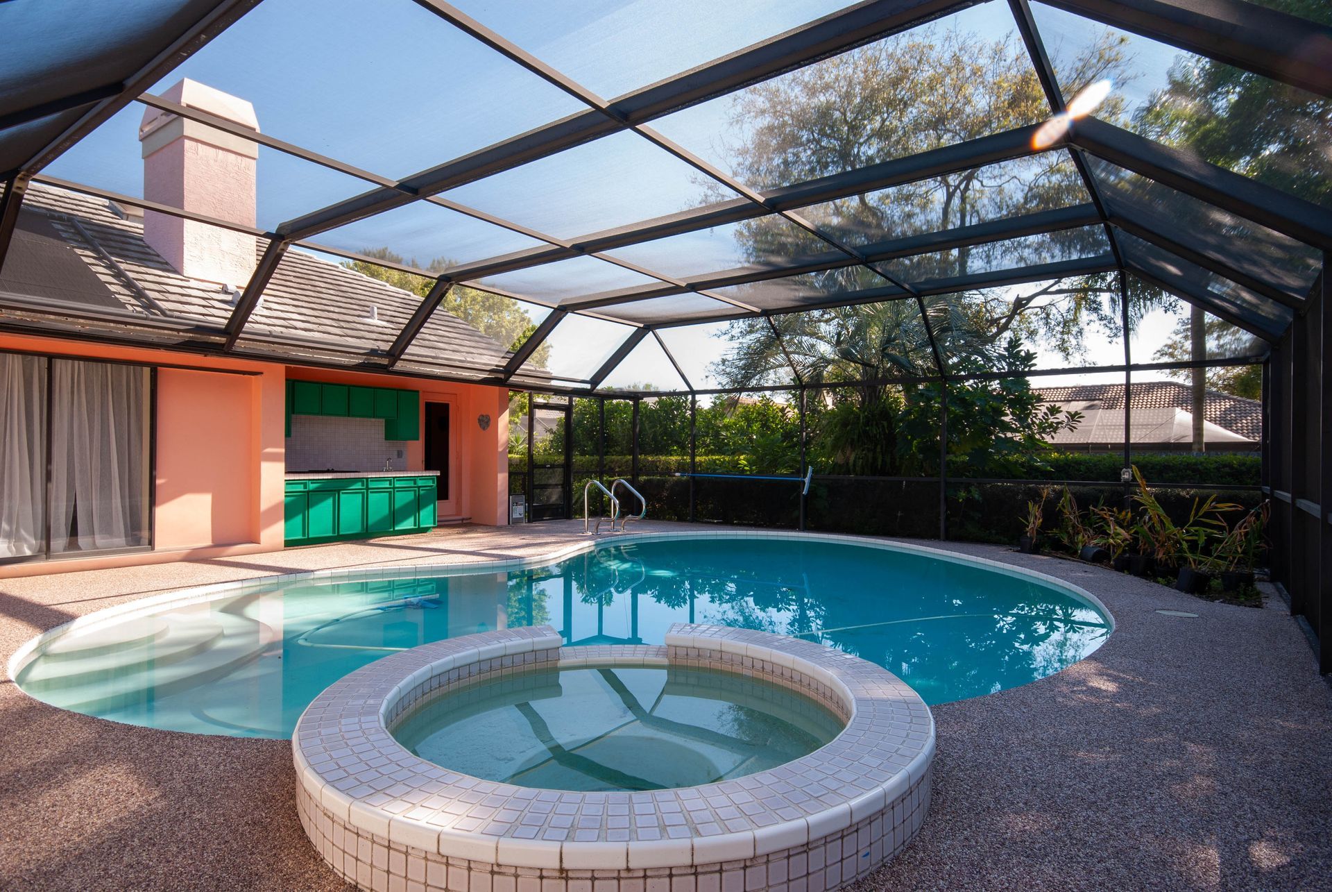 A covered swimming pool and circular hot tub in a backyard patio area with a peach-colored exterior wall. A covered swimming pool and circular hot tub in a backyard patio area with a peach-colored exterior wall.