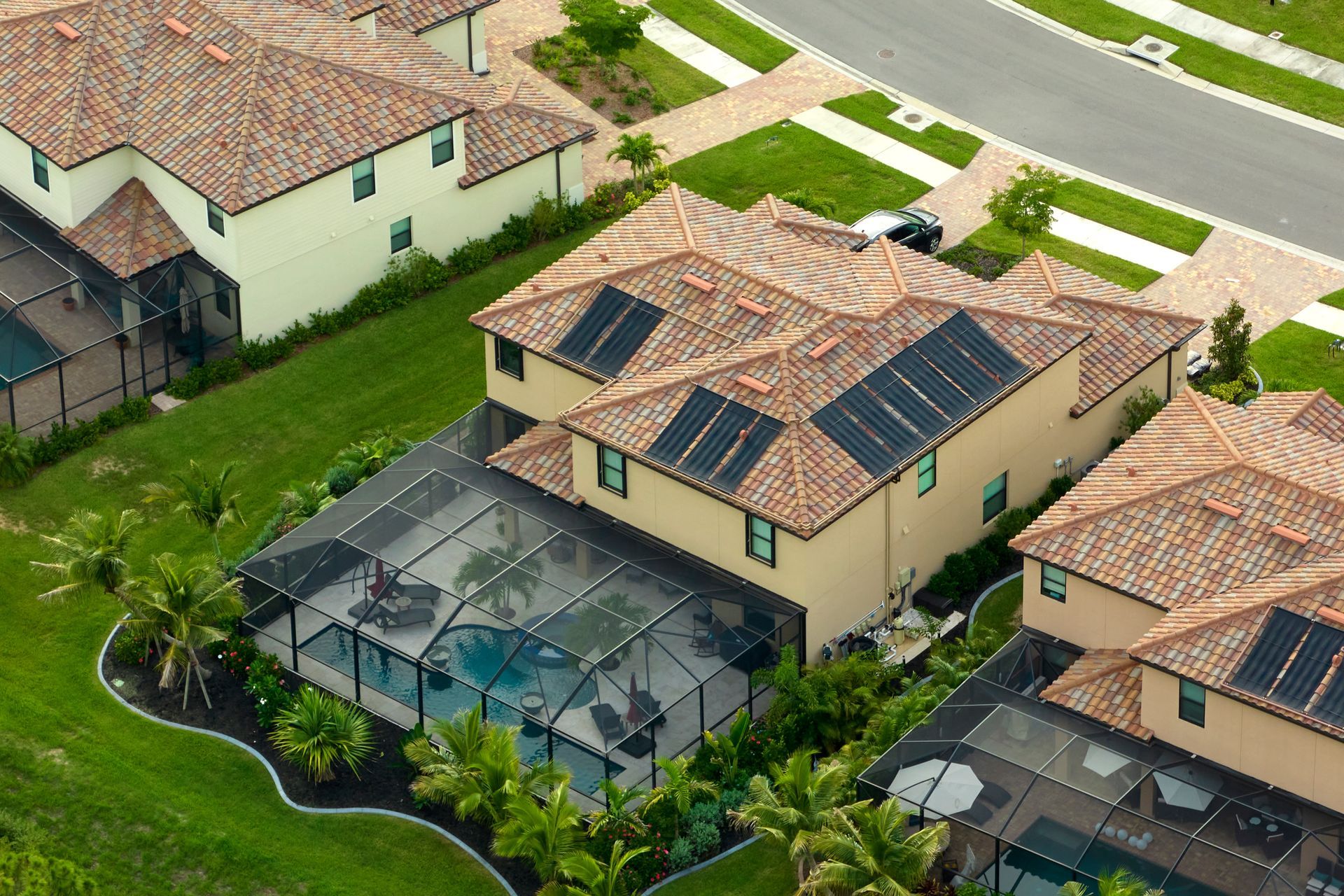 Aerial view of suburban houses with red-tiled roofs, solar panels, and screened-in swimming pools in a residential area. Aerial view of suburban houses with red-tiled roofs, solar panels, and screened-in swimming pools in a residential area.