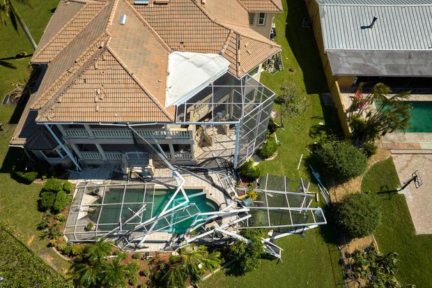 An aerial view of a house with a damaged pool screen enclosure following a storm.