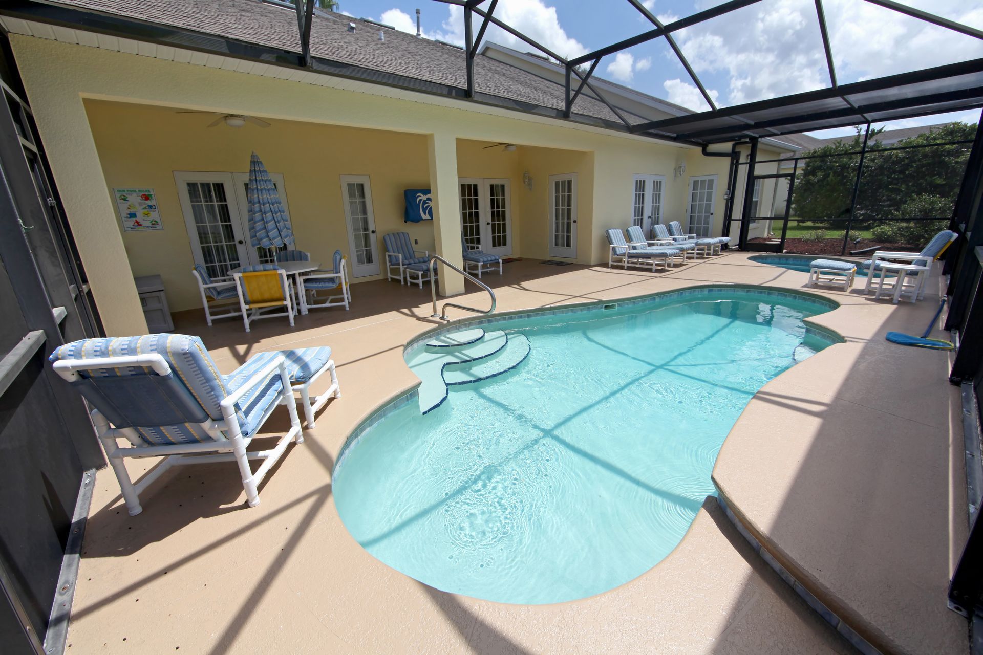 A sunlit, screened-in patio featuring a kidney-shaped swimming pool, lounge chairs, and an outdoor dining set.