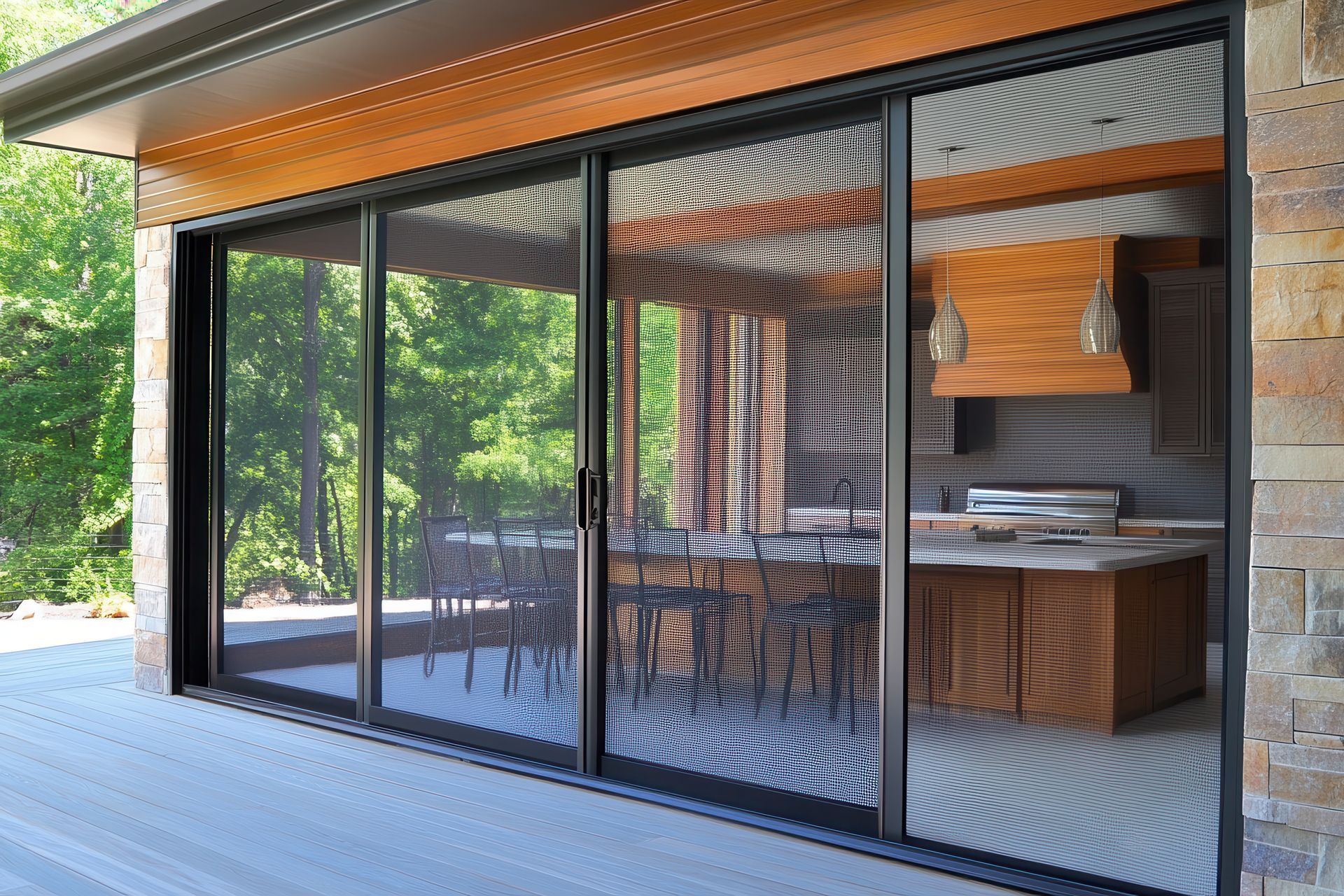 Large sliding glass doors with dark mesh screens open to a stone-walled outdoor kitchen with a wooden ceiling.