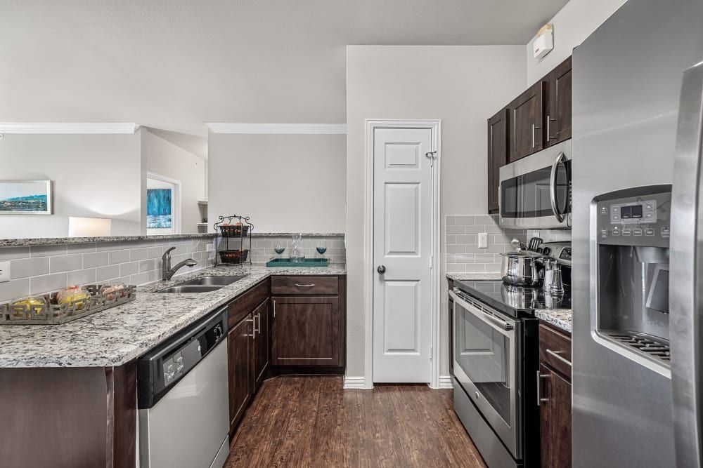 Apartment kitchen with stainless steel appliances, granite counter tops, and dark brown cabinets at Marquis at Silver Oaks in Grapevine, TX.