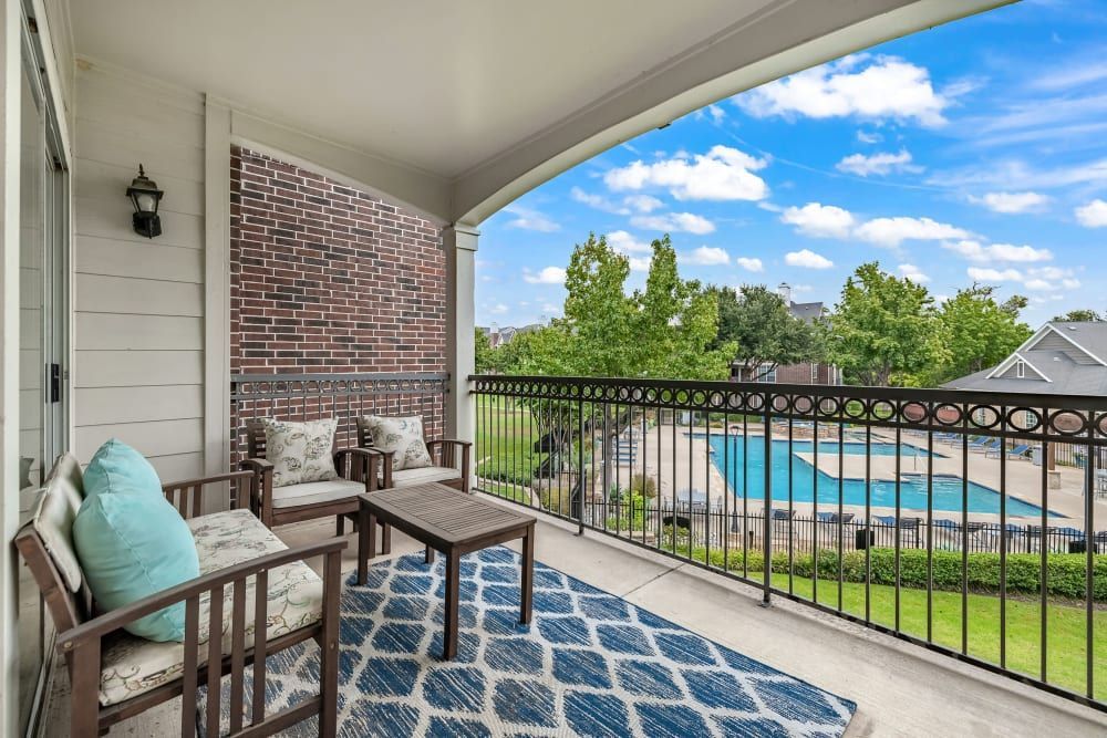Apartment balcony with chairs and a table overlooking the community pool at Marquis at Silver Oaks in Grapevine, TX.