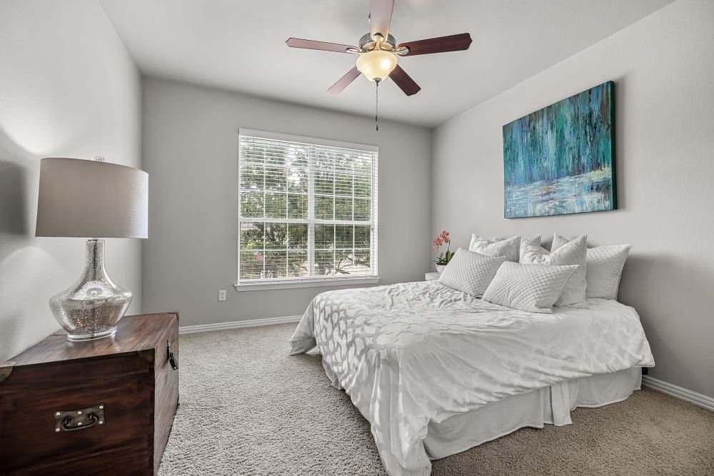 Apartment bedroom with a bed, nightstand, lamp, and ceiling fan at Marquis at Silver Oaks in Grapevine, TX.