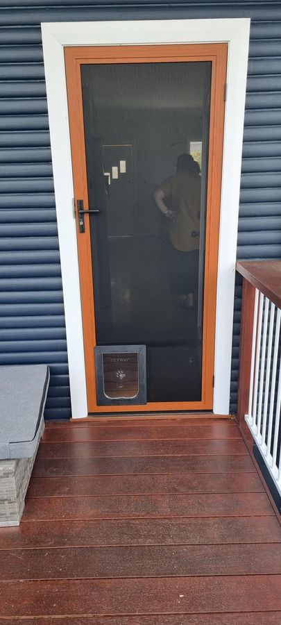 A Screen Door With A Cat Door Is On A Wooden Deck — Nambucca Glass in Nambucca Heads, NSW