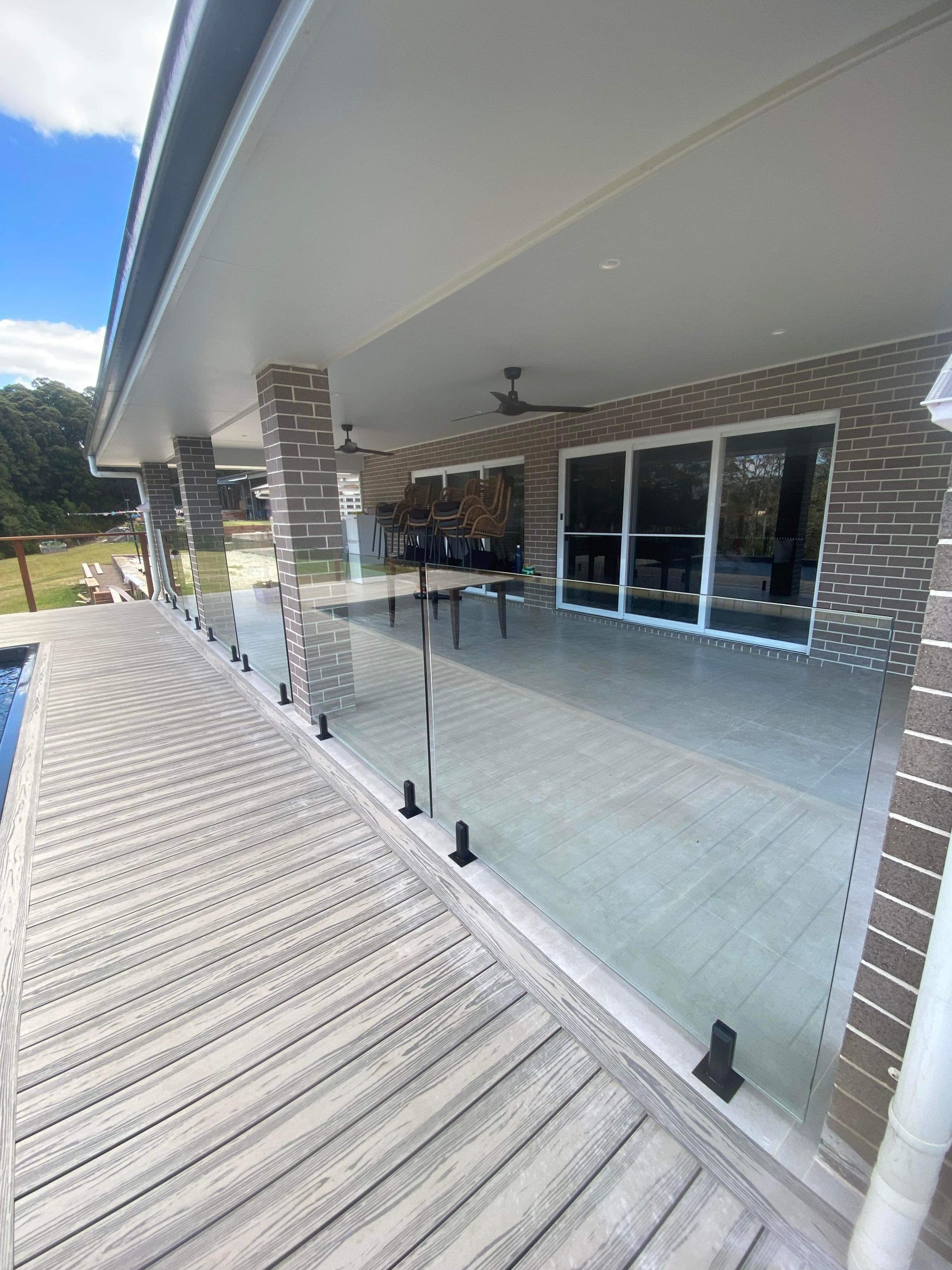 A Patio With A Glass Railing And A Table On It Next To A Pool — Nambucca Glass in Nambucca Heads, NSW