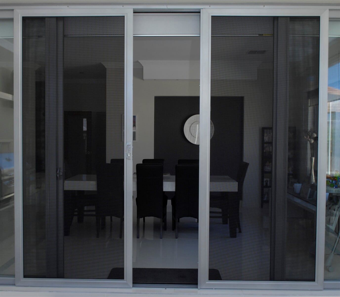A Dining Room With A Table And Chairs Behind A Sliding Glass Door — Nambucca Glass in Nambucca Heads, NSW