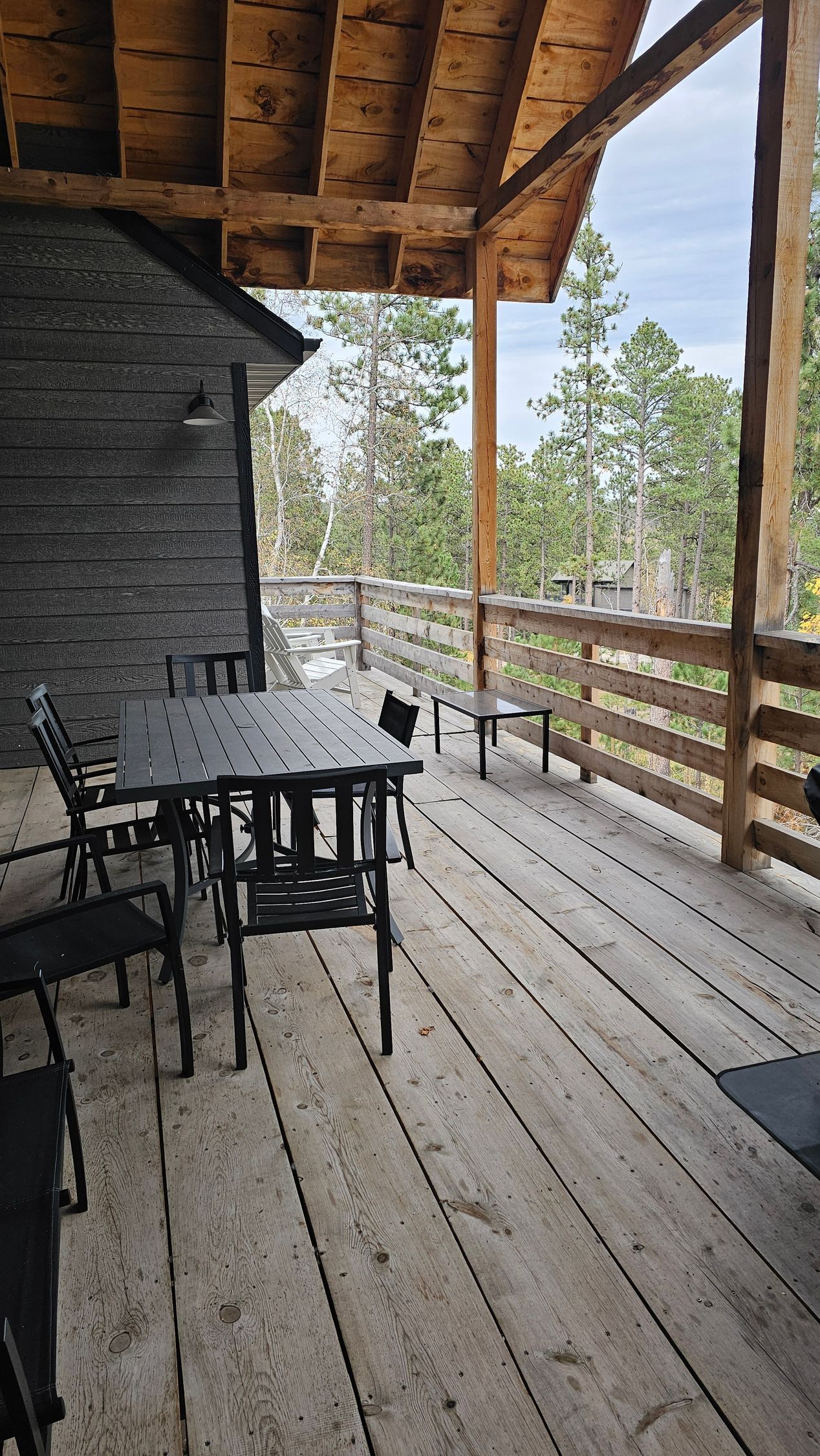 Wooden deck with black furniture, overlooking trees and sky.