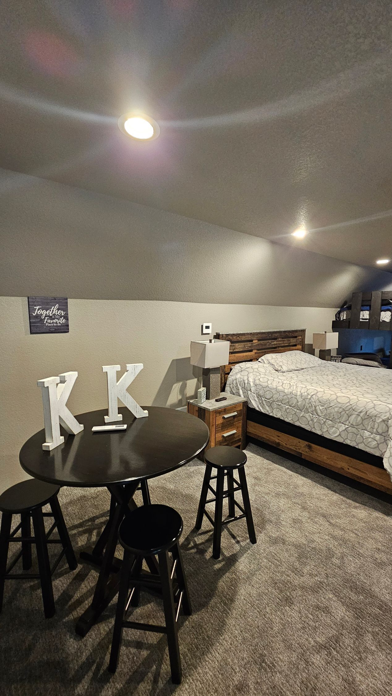 Small bedroom with round table, stools, bed, and slanted ceiling.
