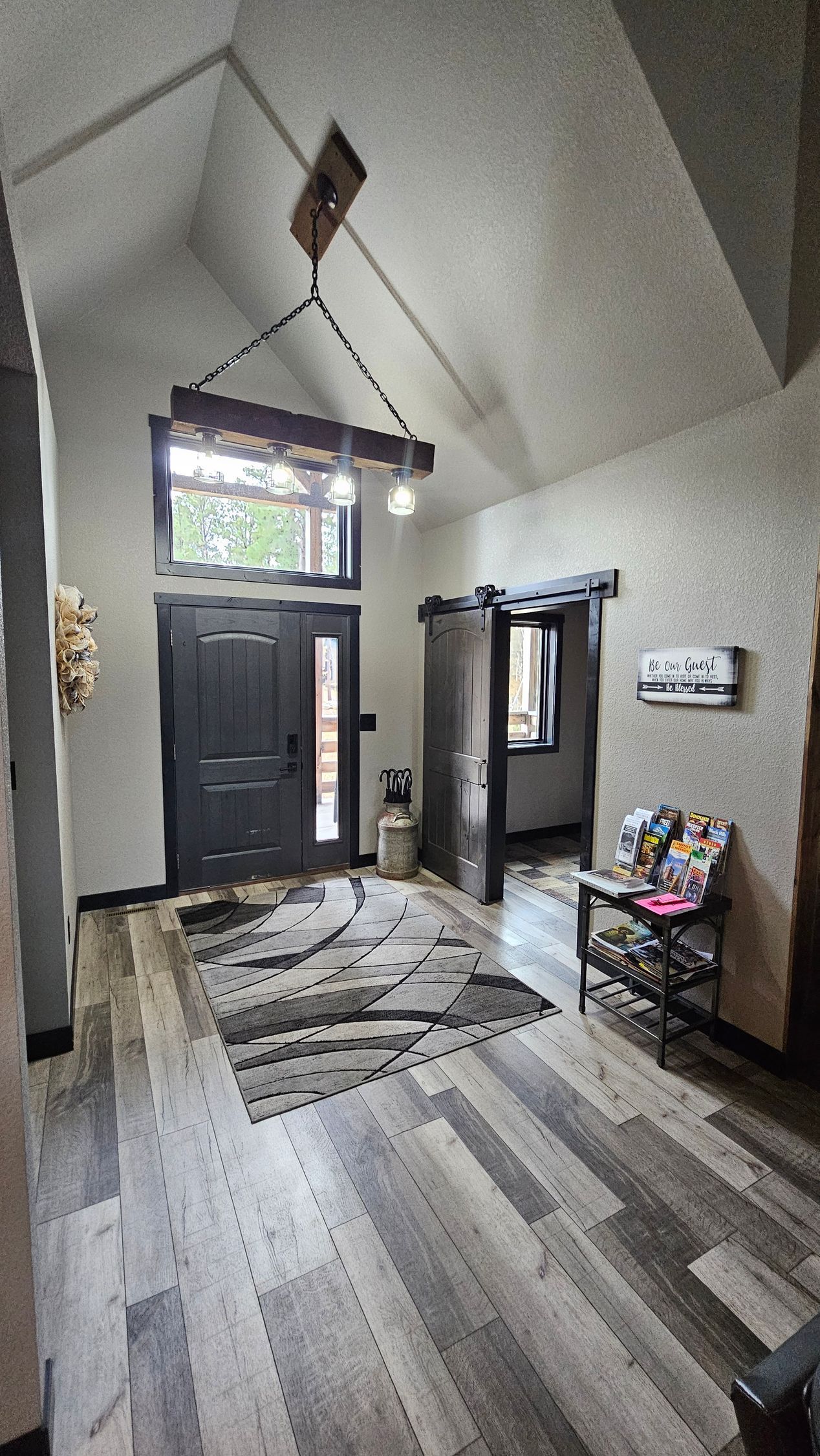 Entryway with dark gray door, wooden flooring, vaulted ceiling, and decorative wooden chandelier.