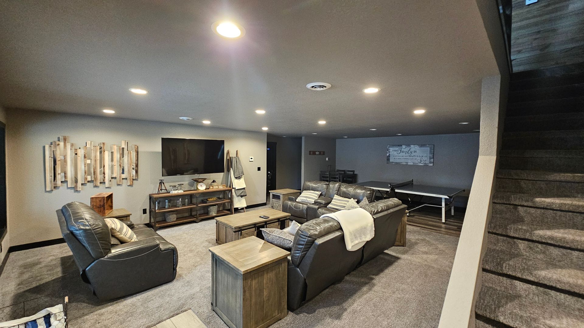 Basement living room with gray couches, TV, wooden accents, and a staircase.