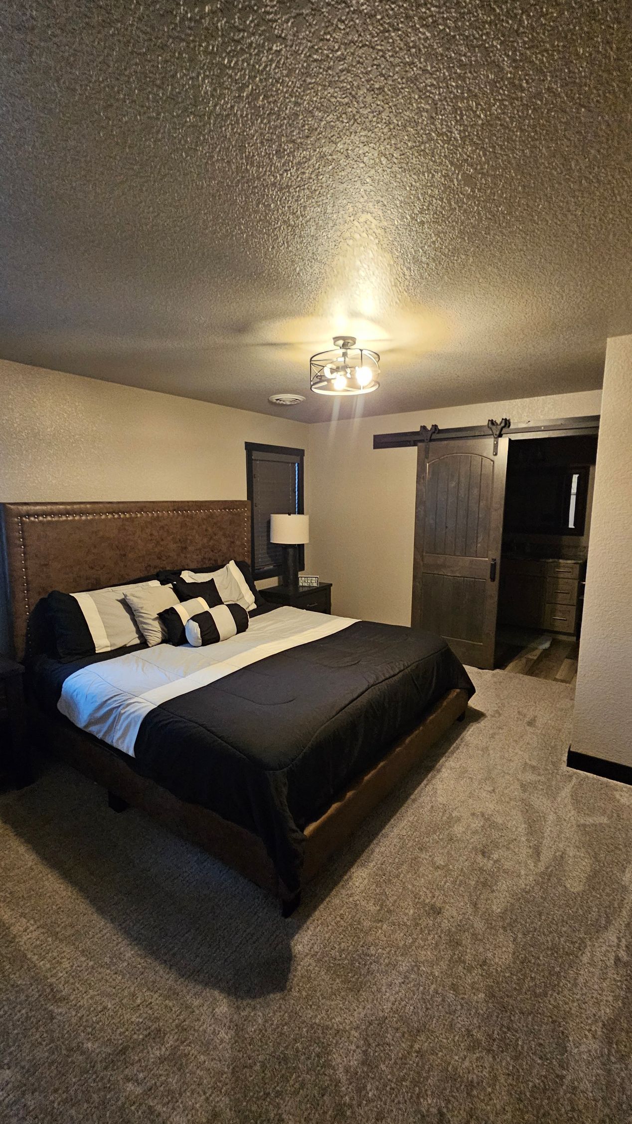 Bedroom with a large bed, dark wood headboard, sliding barn door, and a brown carpet.