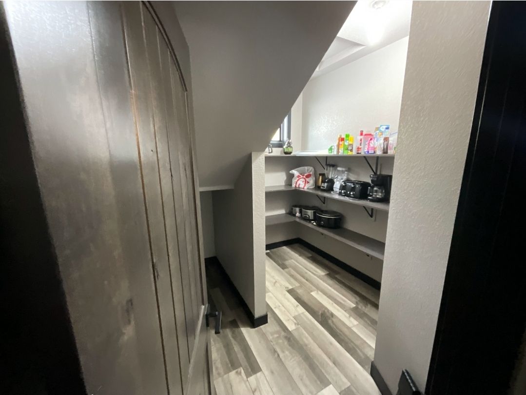 Pantry with wooden floors and shelves stocked with food items. Gray and white interior.