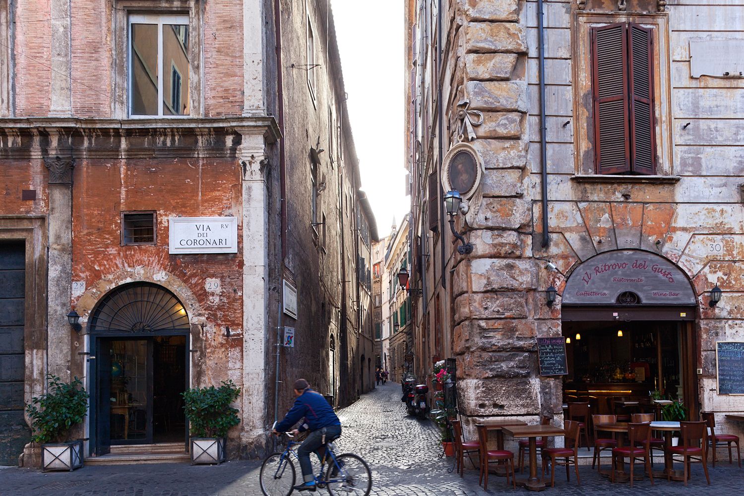 A man is riding a bike down a narrow street between two buildings