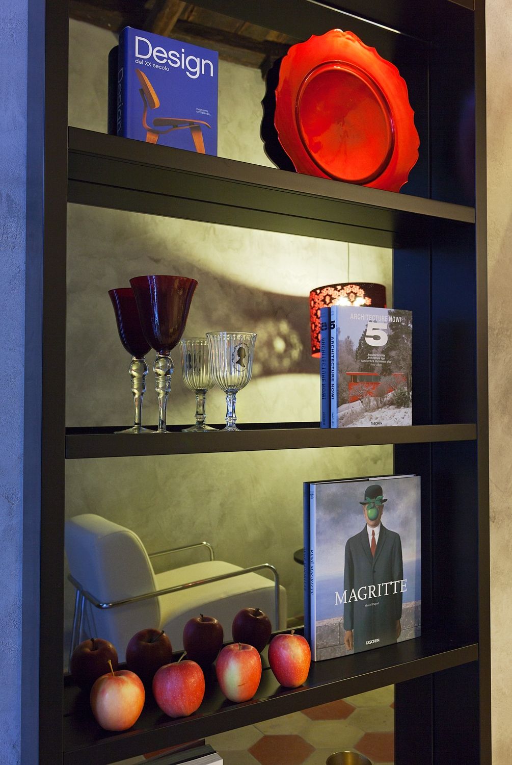 A book called design sits on a shelf with apples and wine glasses