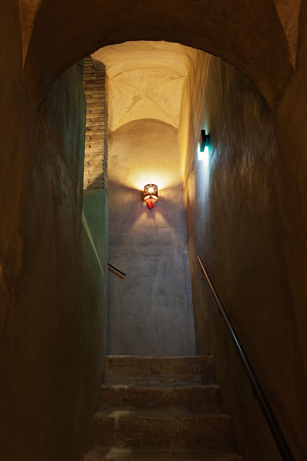 A dark tunnel with stairs and a light on the wall