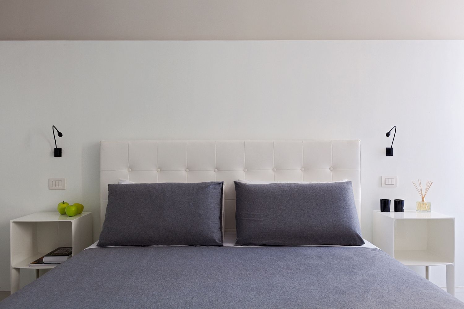 A bed with a white headboard and grey pillows in a bedroom