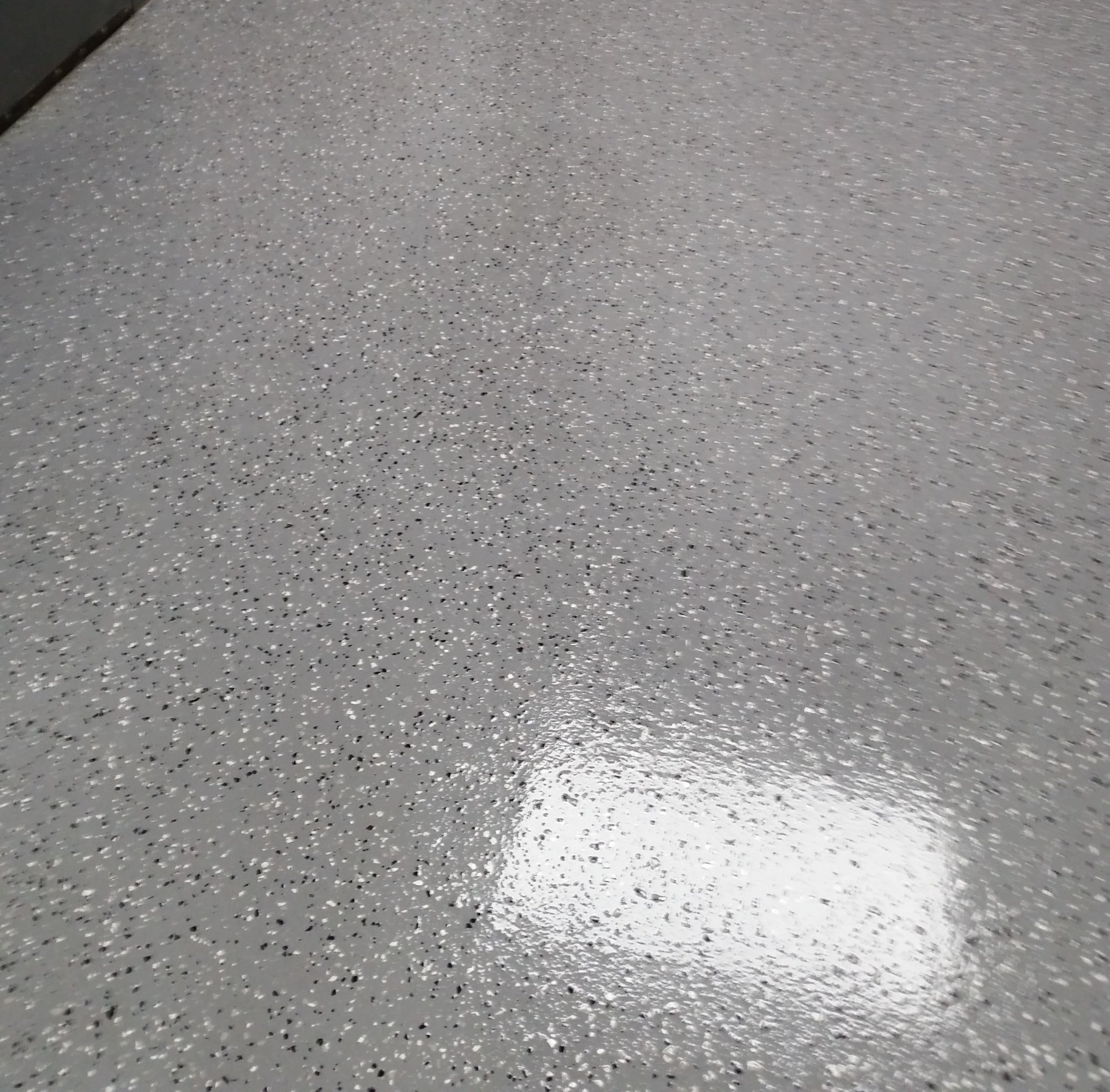 Sol recouvert d'époxy, parsemé de paillettes grises, noires et blanches. La lumière se reflète sur une surface brillante.