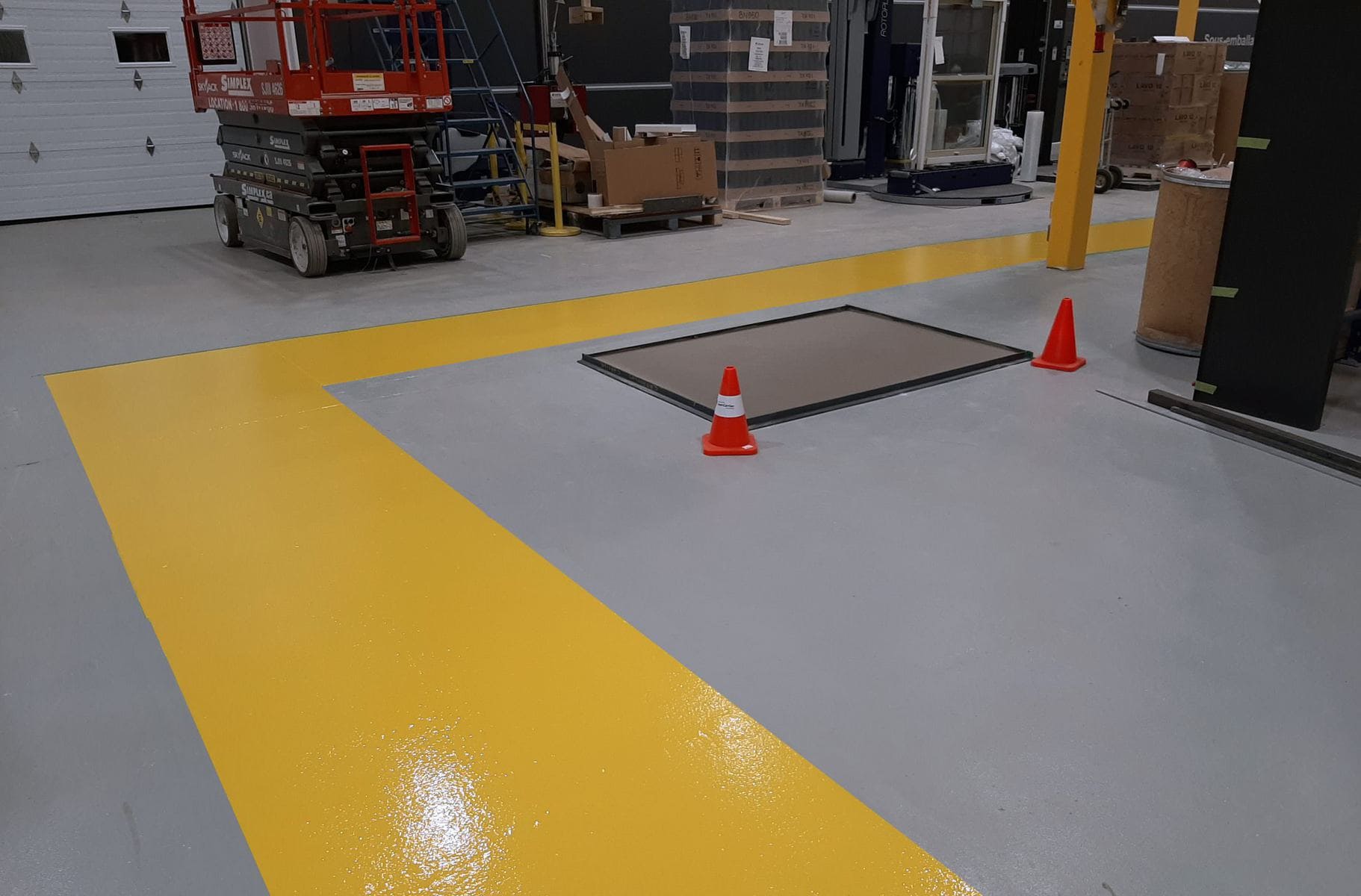 Un entrepôt avec un sol jaune et gris et une bande jaune sur le sol.