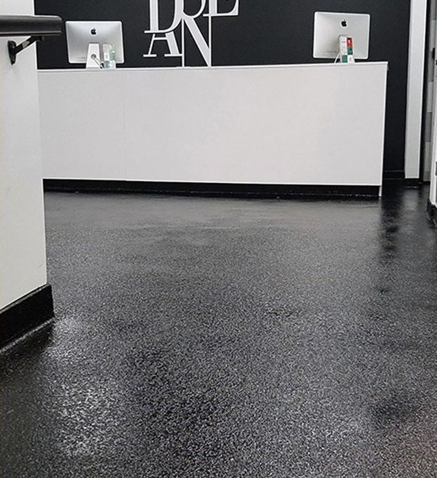 Hall d'entrée vide avec une réception blanche, des murs noirs et un sol sombre moucheté.
