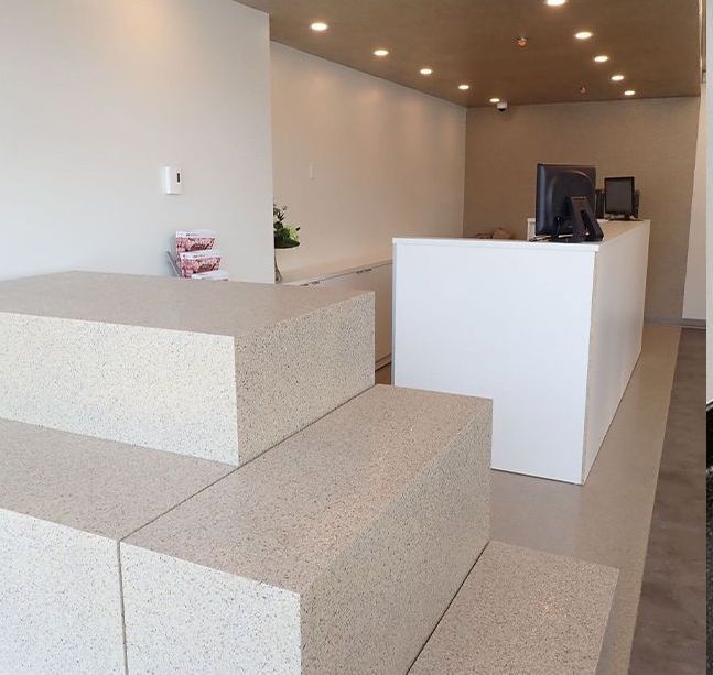 Espace d'accueil moderne avec bureaux blancs, banquettes en pierre et éclairage encastré au plafond
