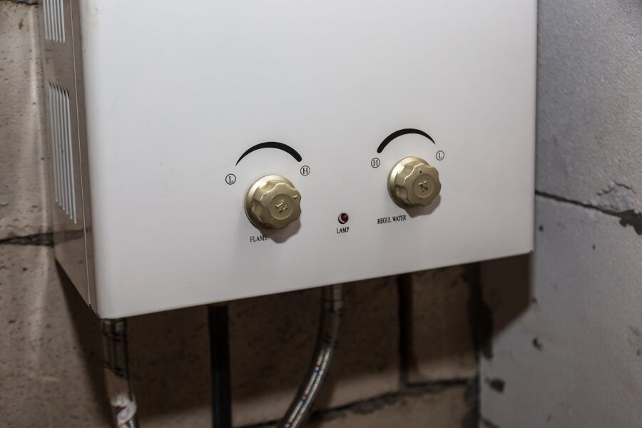 A white water heater is hanging on a brick wall.