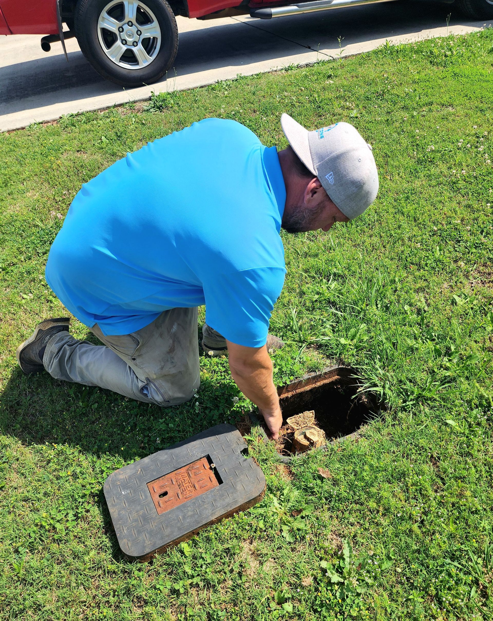 A man is kneeling down in the grass looking into a hole in the ground.