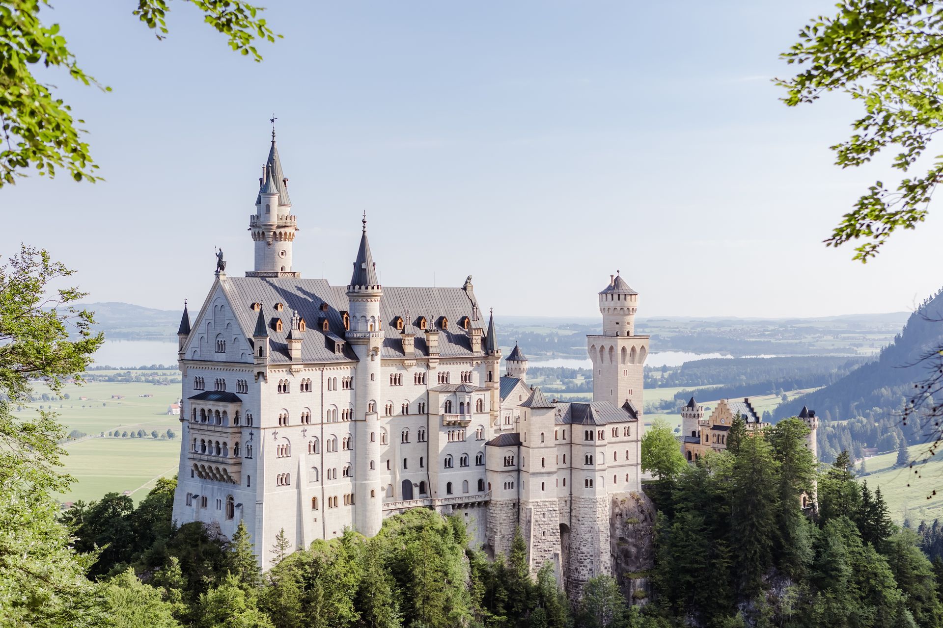 Neuschwanstein Castle, Germany, white fairytale castle atop green hillside, clear sky.