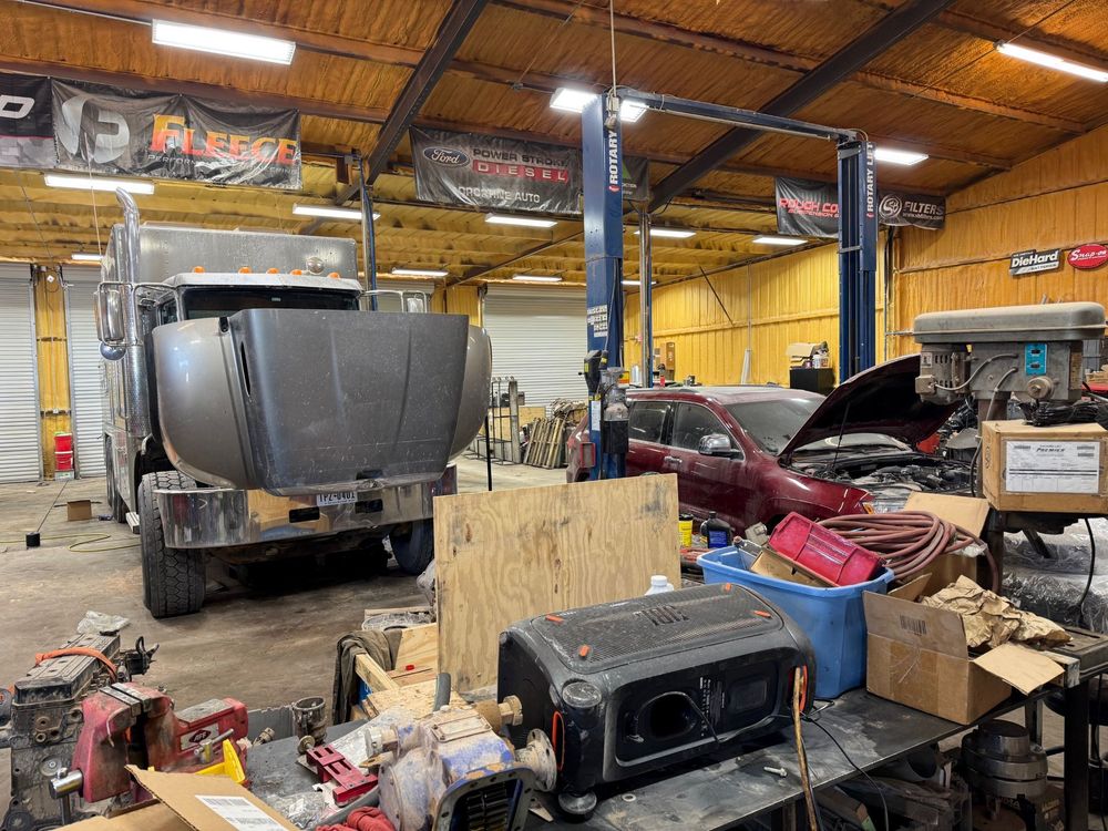 Auto repair shop with a truck, open car hood, and scattered tools under a high metal roof