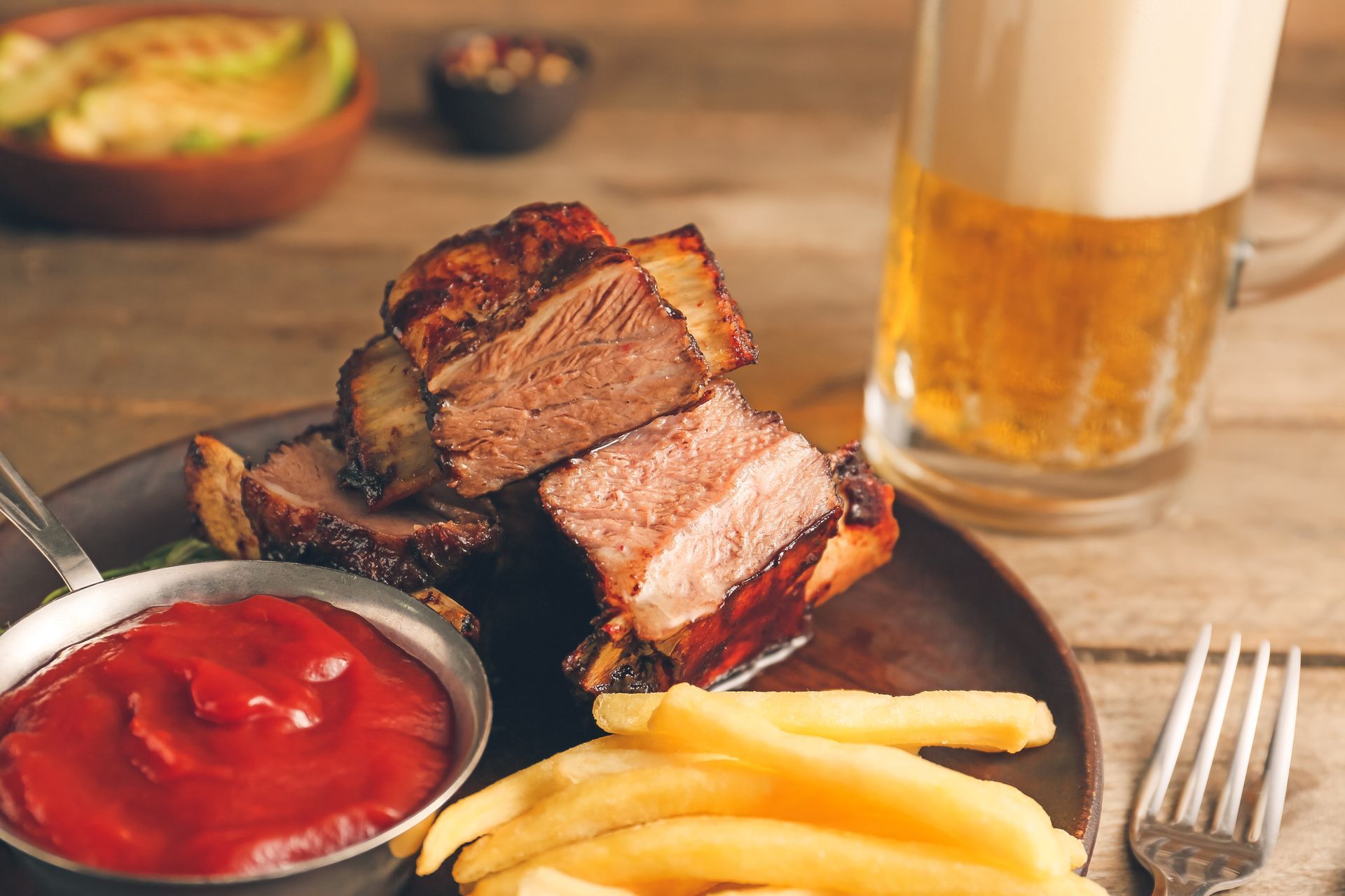 Steak with fries and ketchup beside a glass of beer on a table