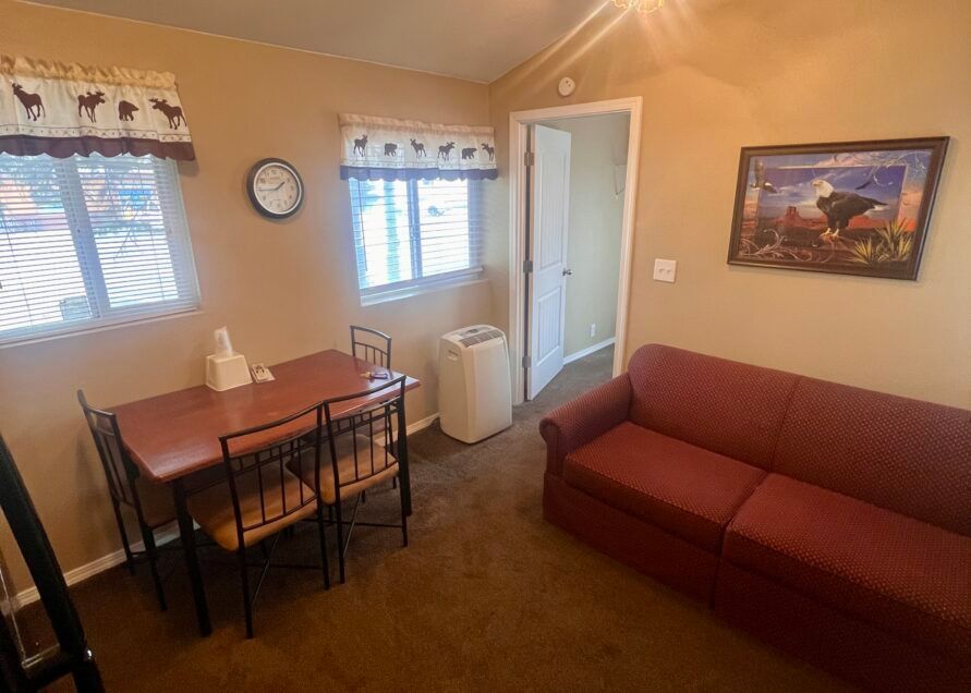 A small room with a red sofa, dining table, and a doorway. A clock and a framed picture are on the walls.