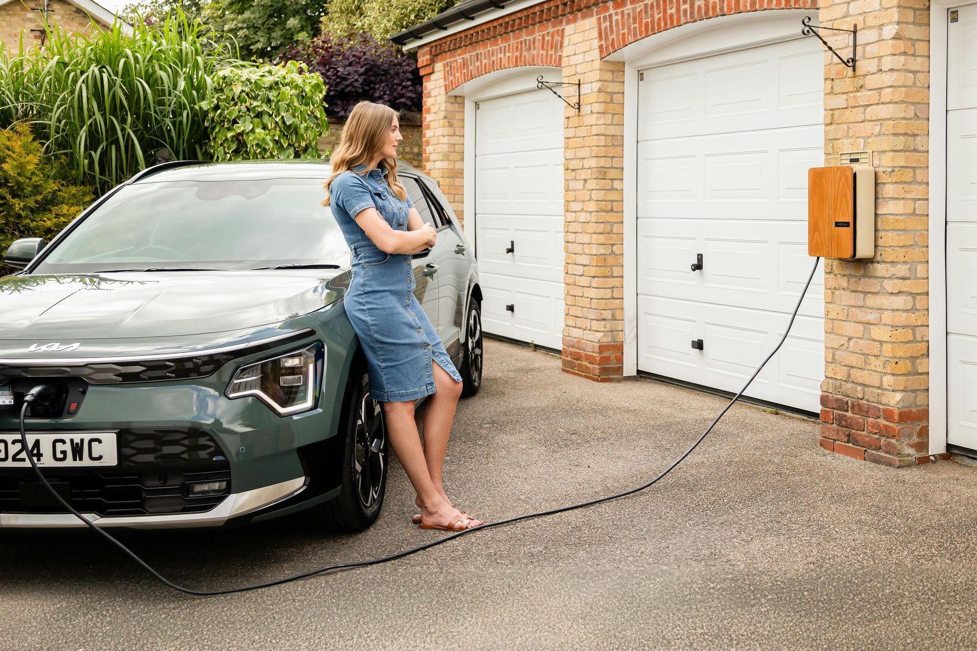 Woman charging an electric SUV in a driveway beside a brick garage