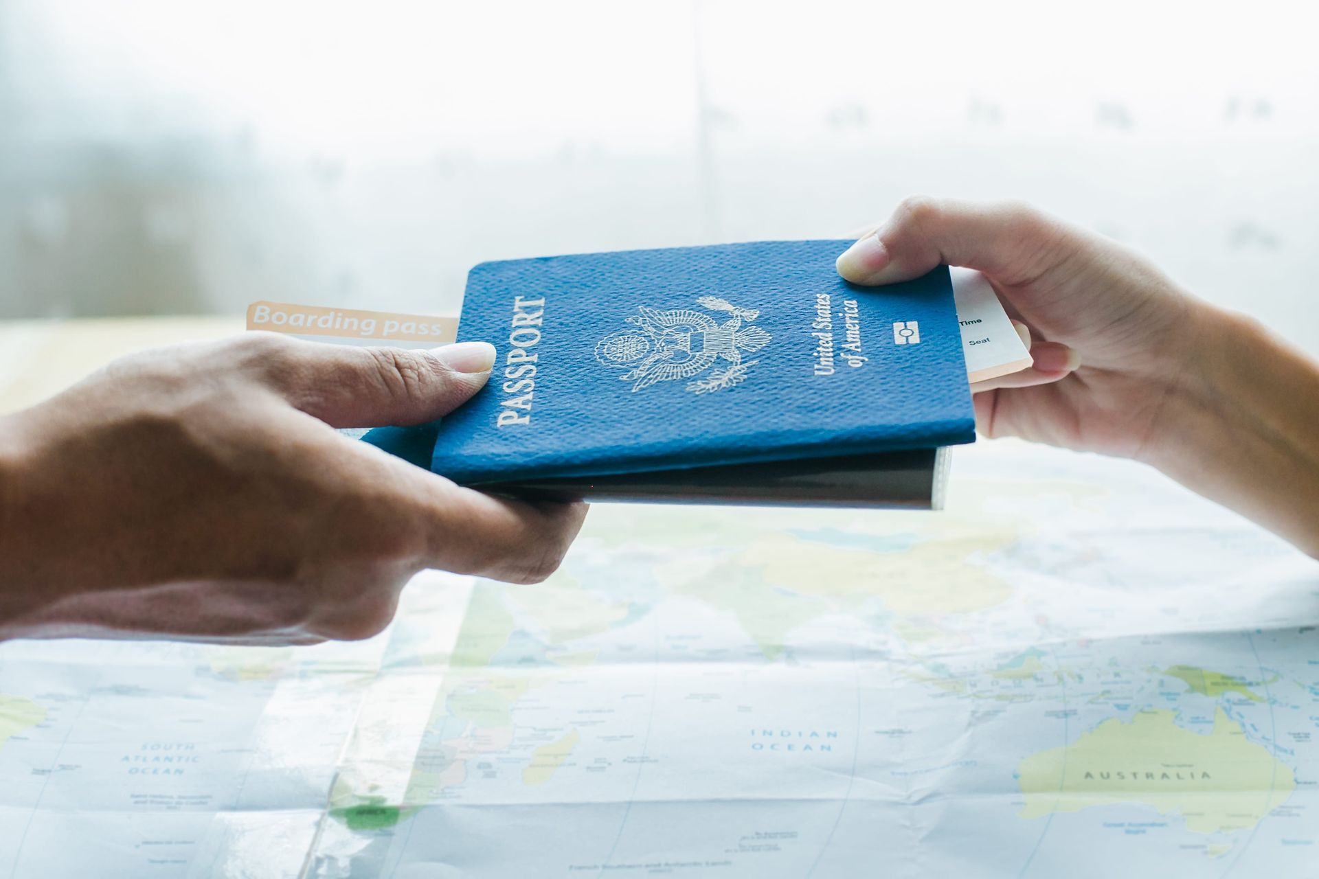 Two hands exchange a blue passport over a world map.
