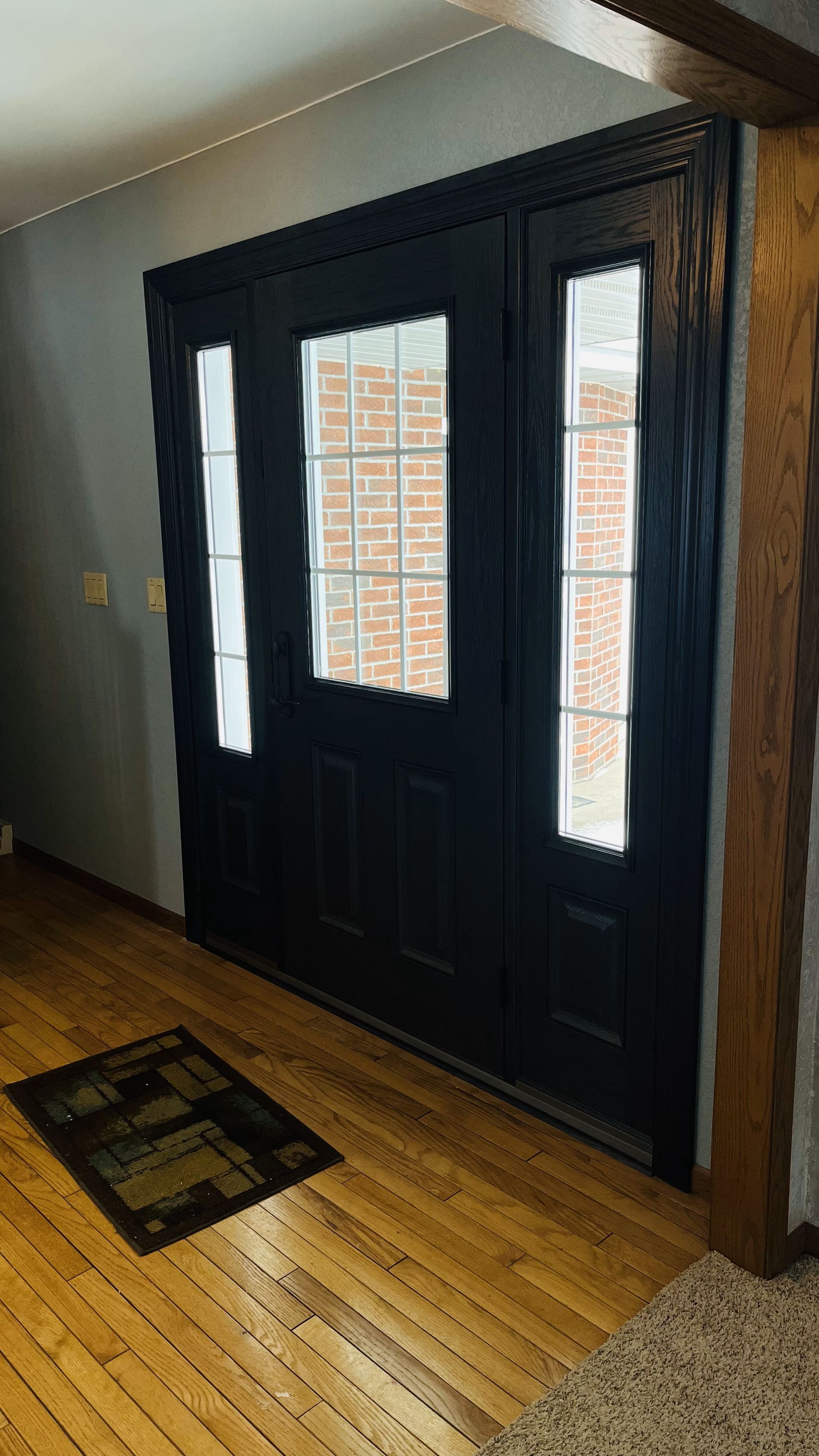 Black front door with sidelights, wooden trim, and a small welcome mat.