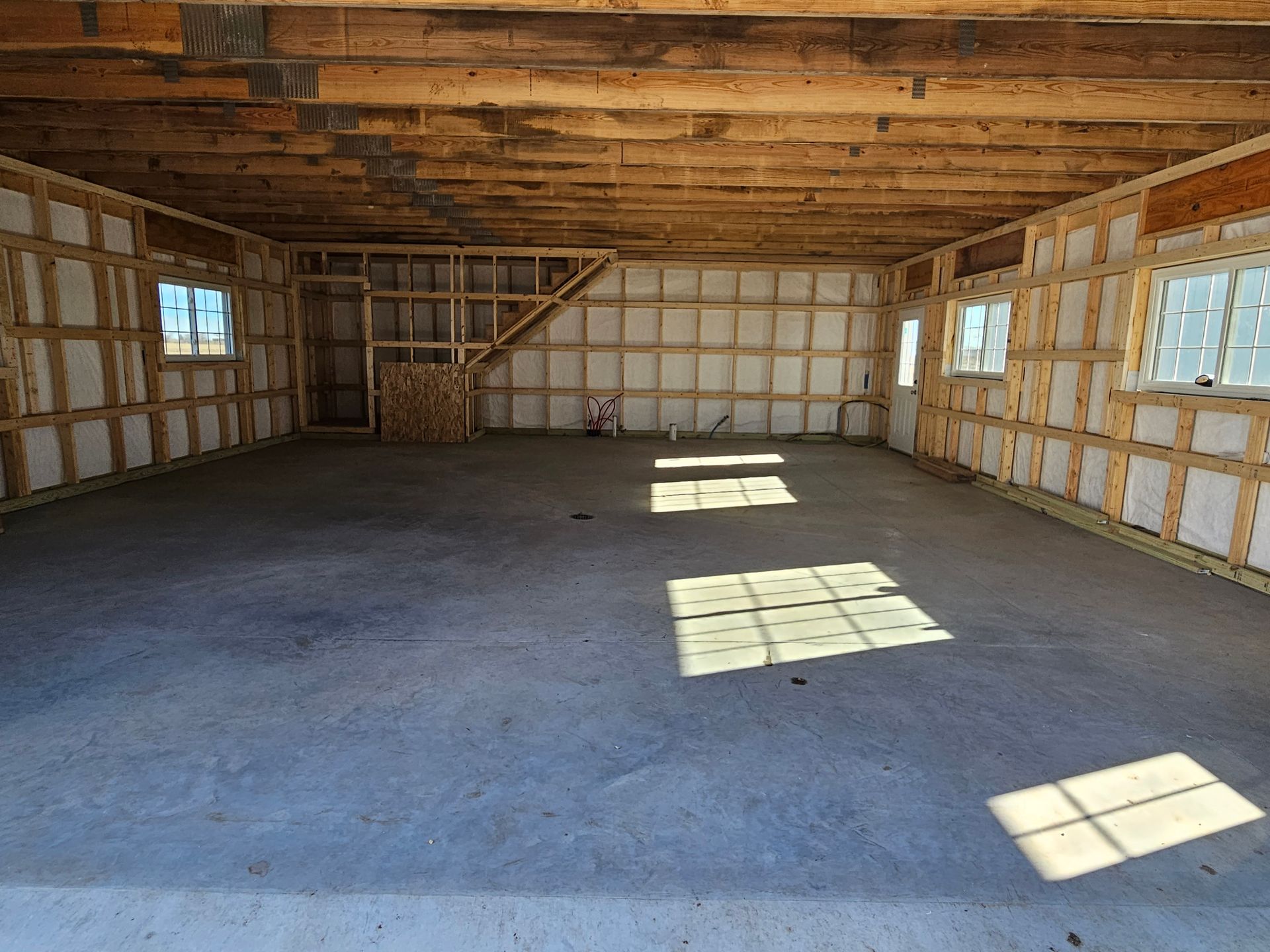 A large empty garage with concrete floors and wooden beams.