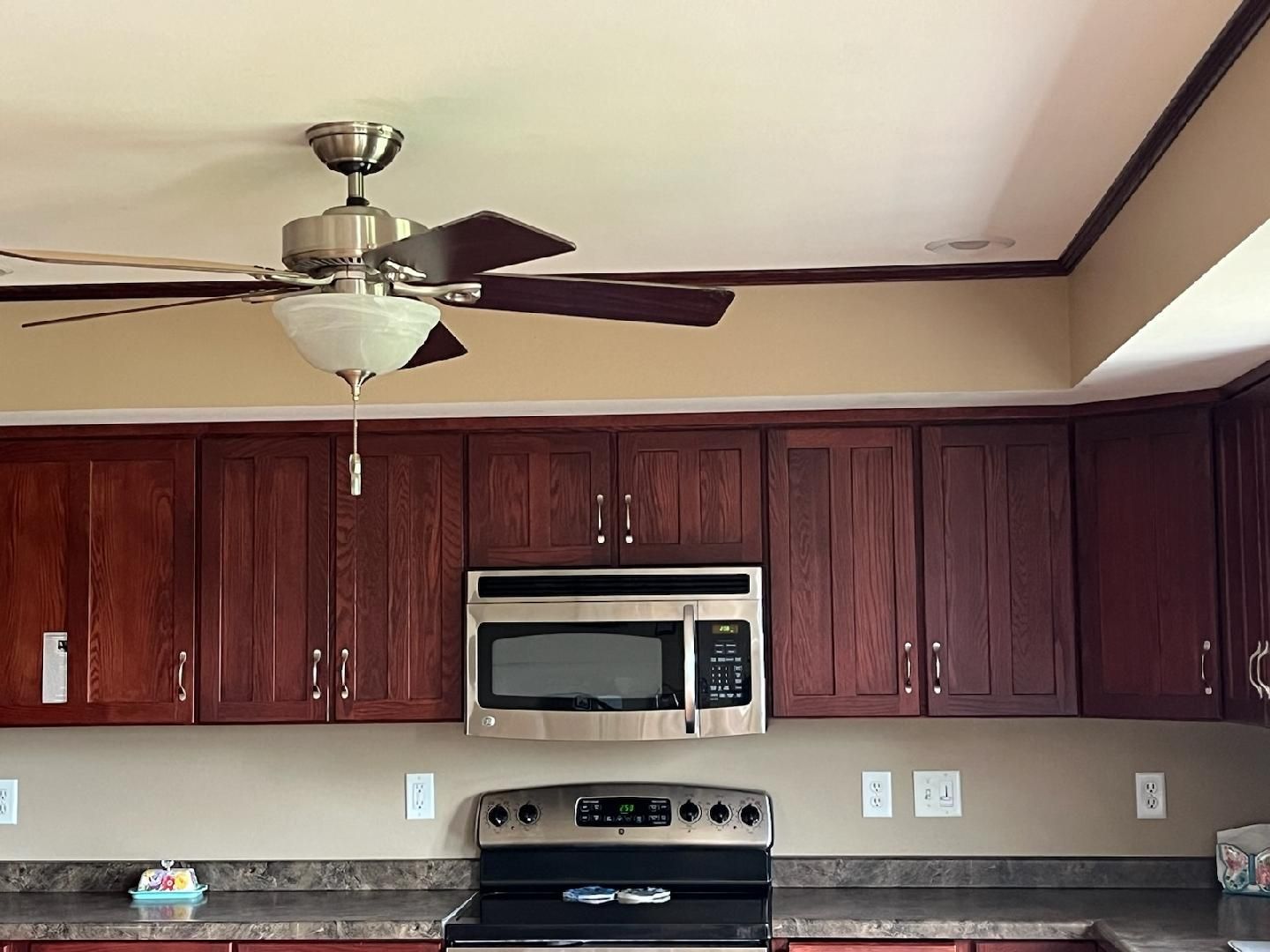 Kitchen with brown cabinets, stainless steel microwave, and a ceiling fan.