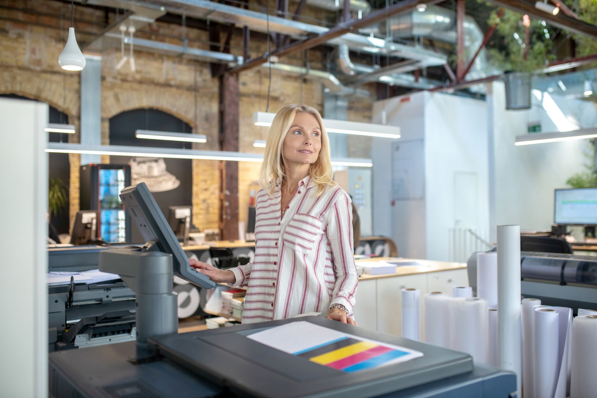 A woman is standing in front of a printer in an office.