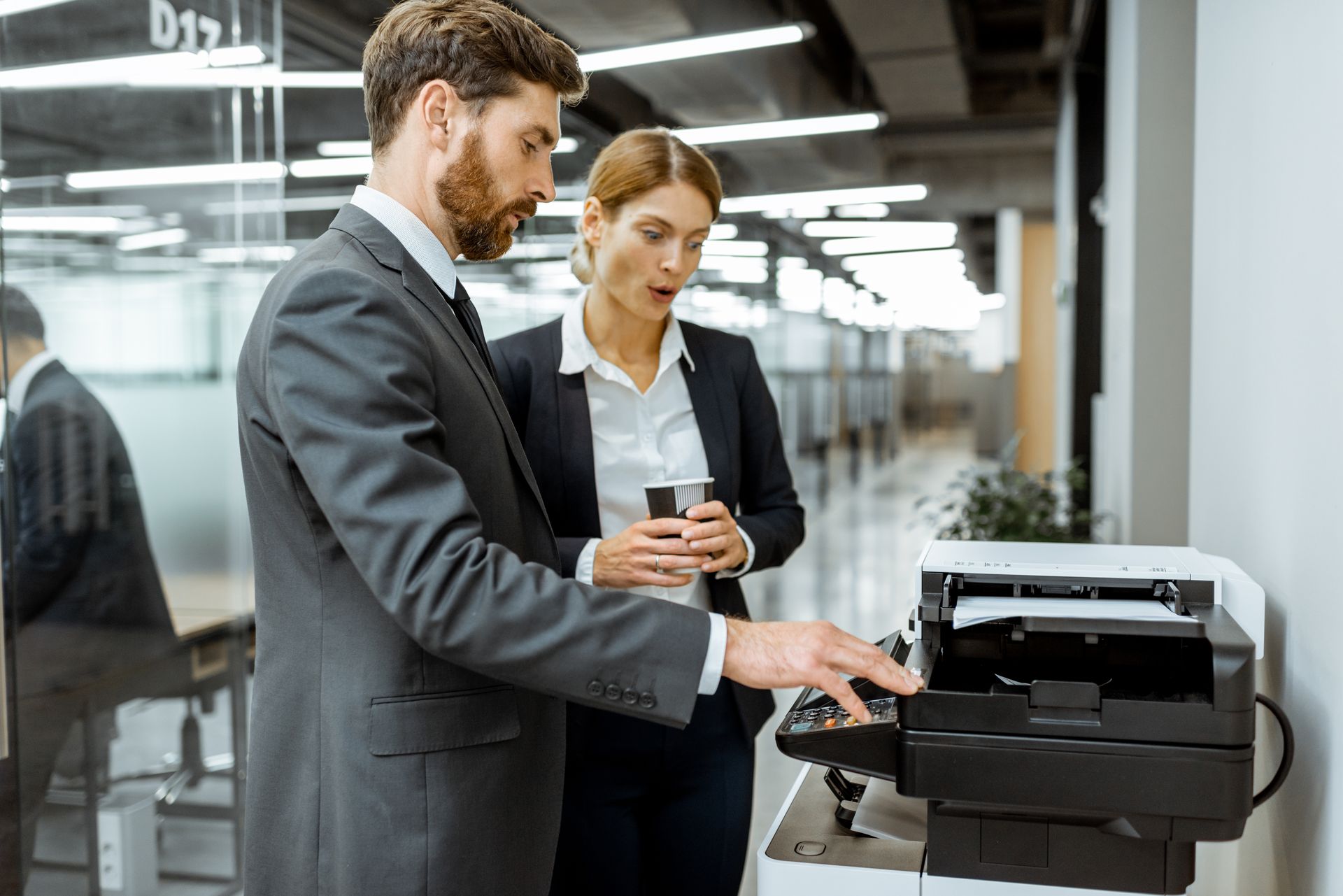 Two office workers checking a black printer in a modern workspace