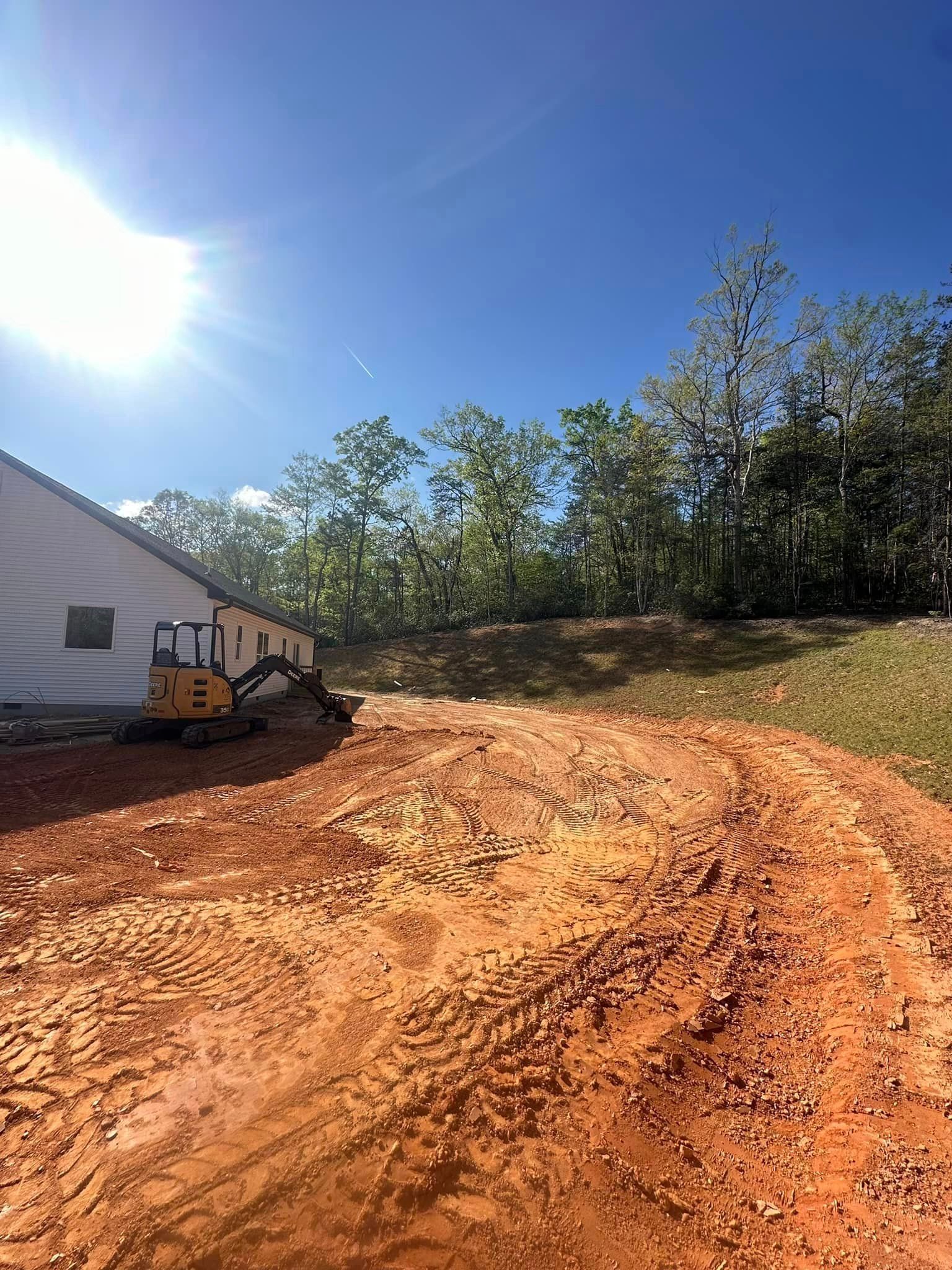A dirt road with a house in the background and a bulldozer on the side of it.