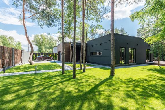 Modern dark building with large windows in a sunny park with green lawn and tall trees